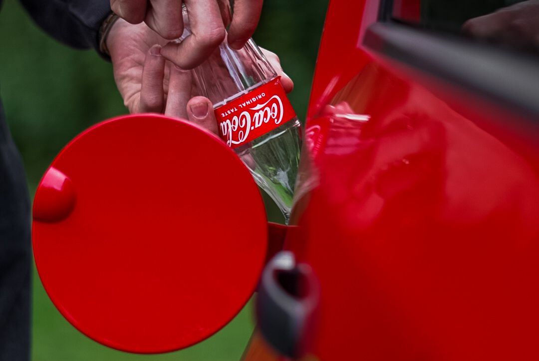 A hand pours a Coca-Cola beverage into a large red circular disc against a green background.