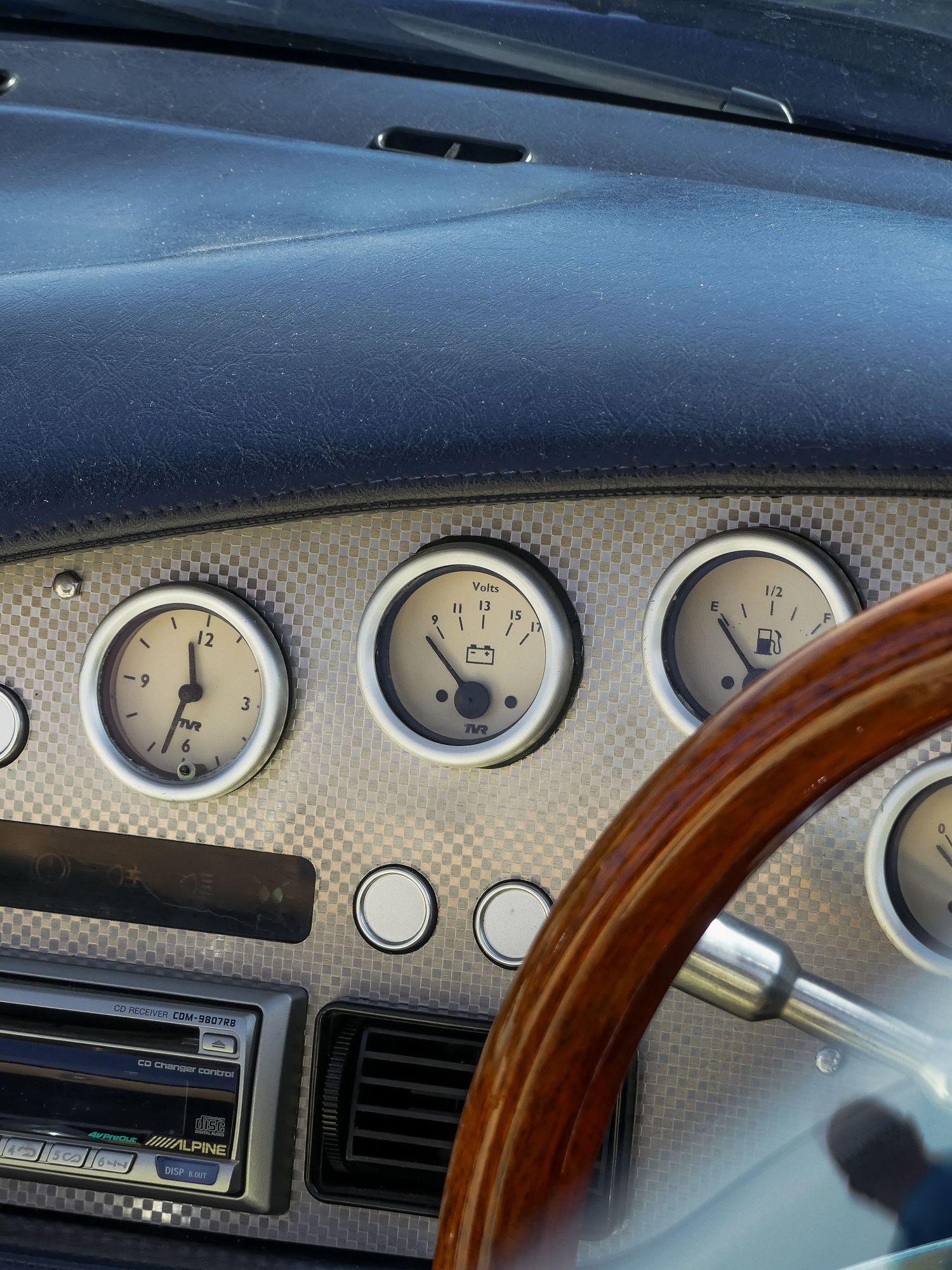 A closeup view of luxury car dashboard gauges with wood trim and carbon fiber accents showing instrument cluster details.