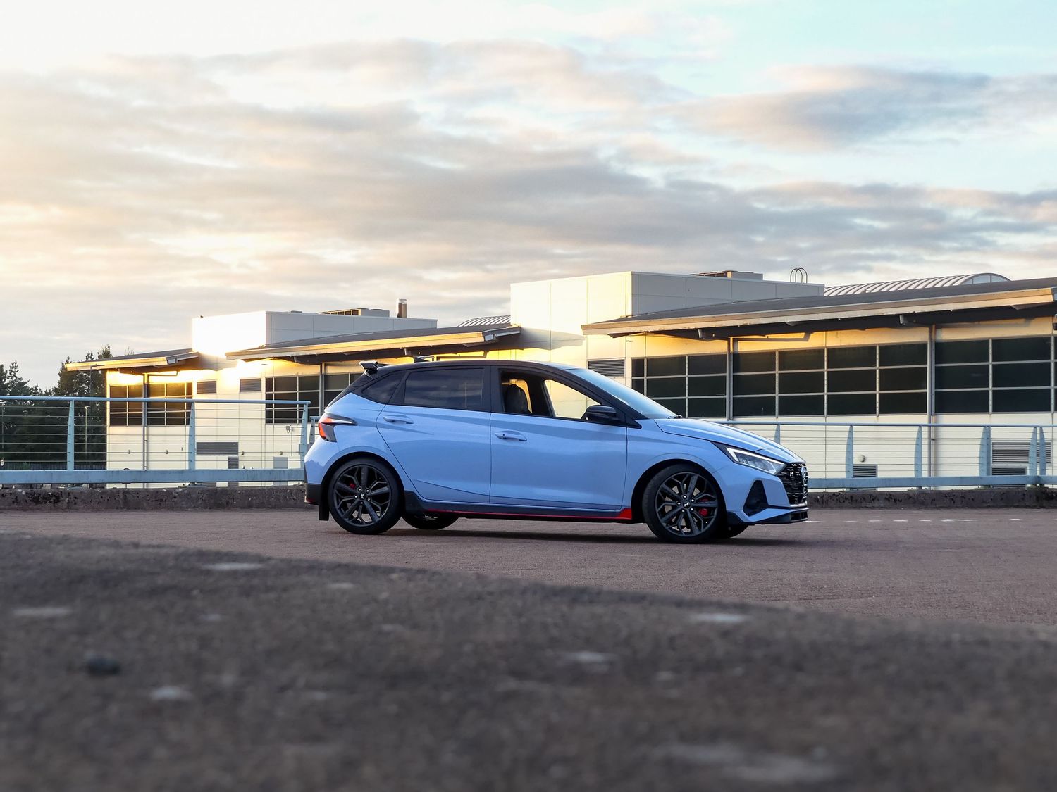 A series of modern cars parked in a row at sunset with dramatic clouds in the sky above.
