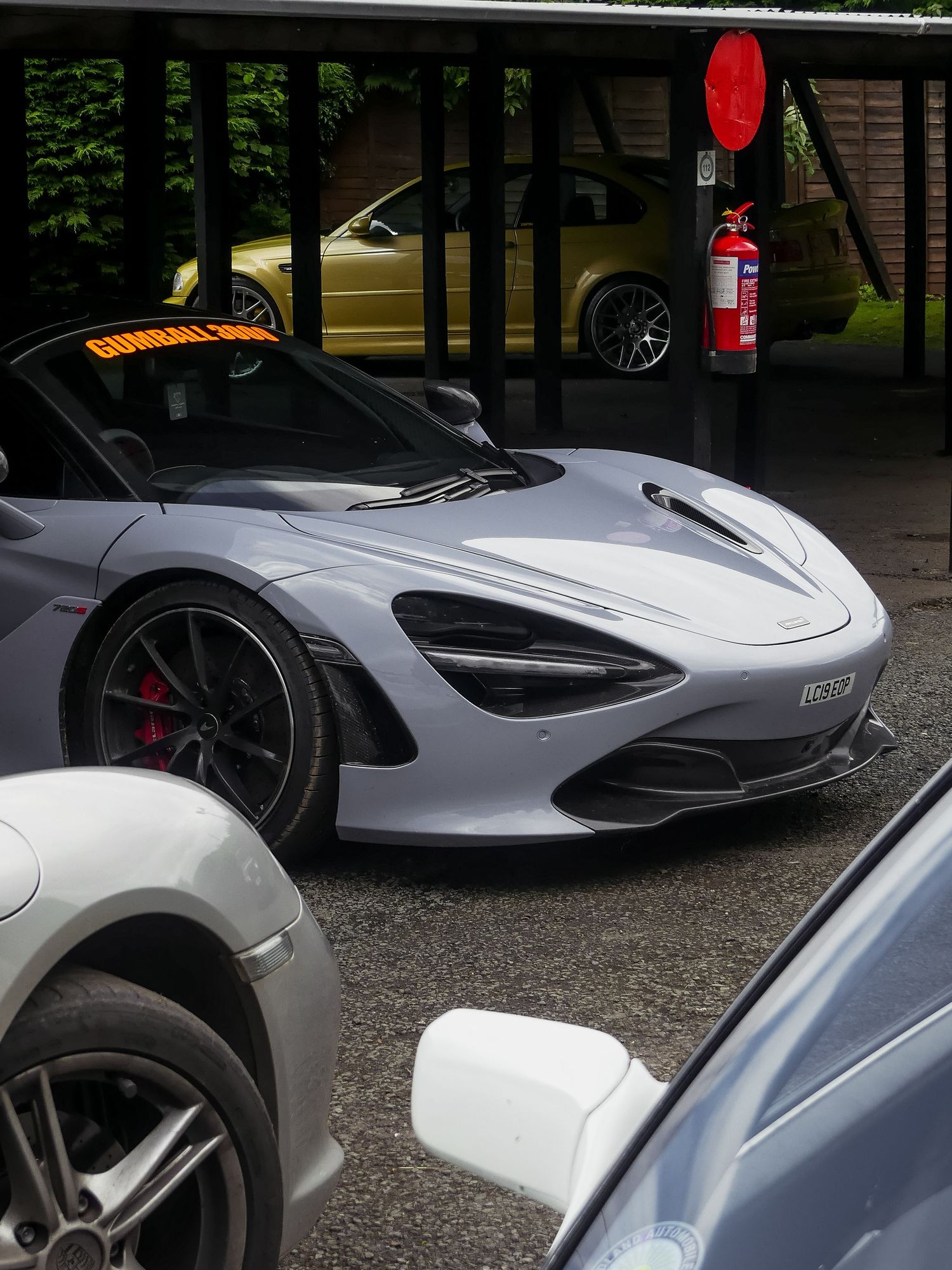 McLaren 720S supercar in silver parked under a carport with a red fire extinguisher mounted on post.