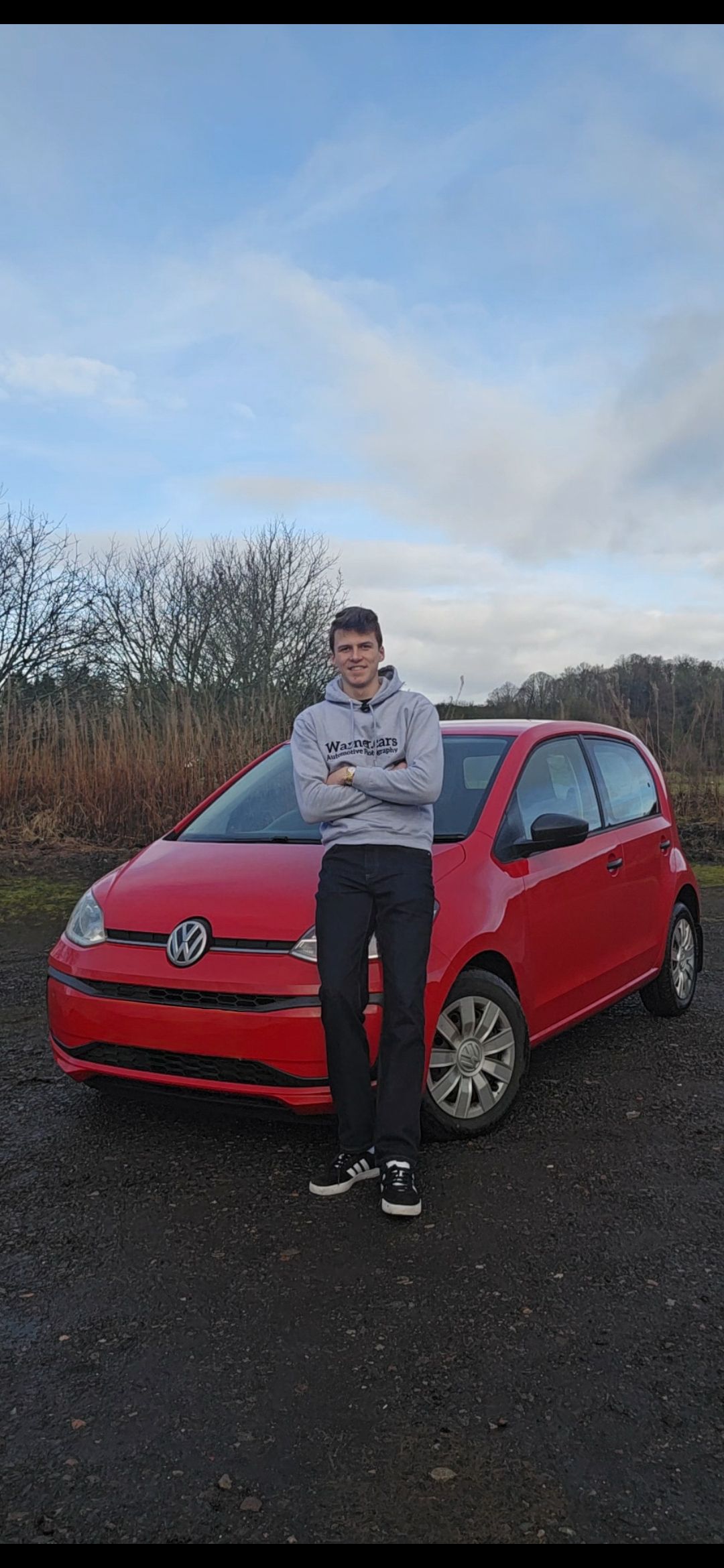 A red Volkswagen Golf parked on dark ground with bare trees in the background on an overcast day.