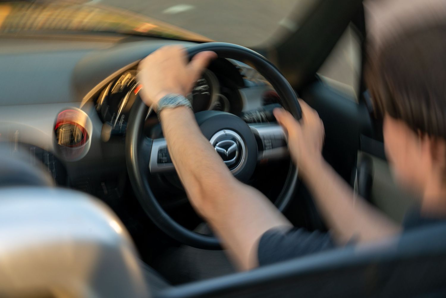 Person gripping a Mazda steering wheel while driving, captured with motion blur effect inside the car.