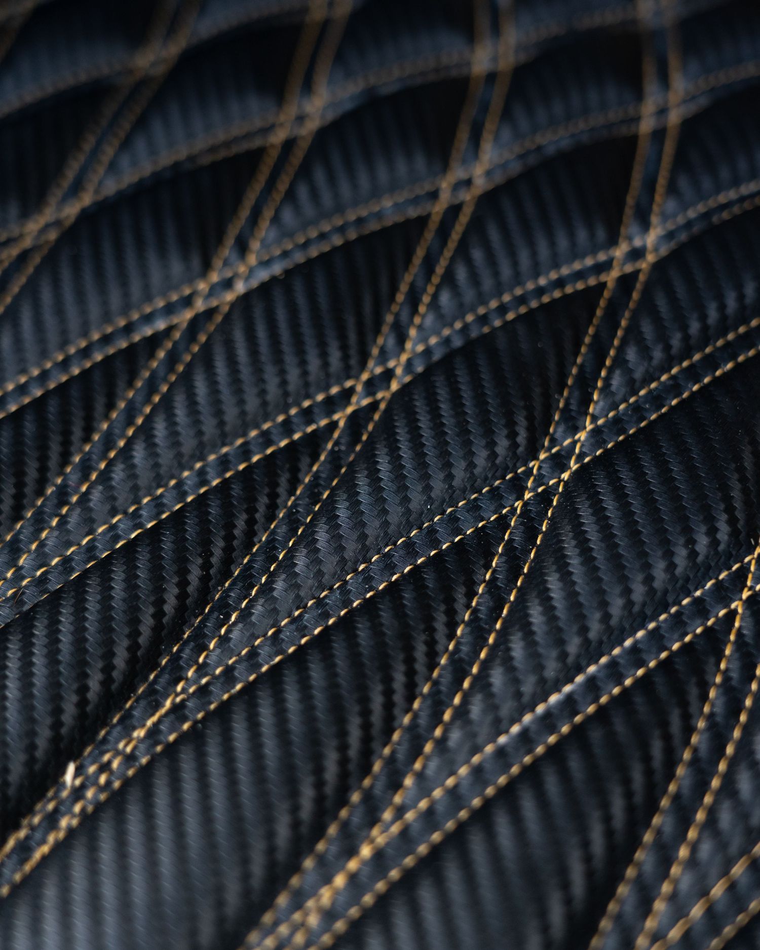 Close-up of black carbon fiber material with diamond quilted pattern and gold stitching detail.