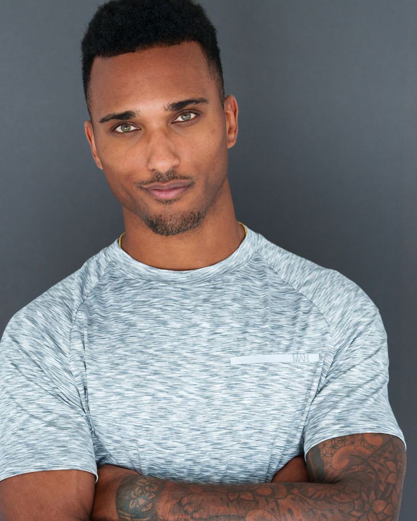 Athletic portraits in heather grey t-shirt showing tattoos against dark background.