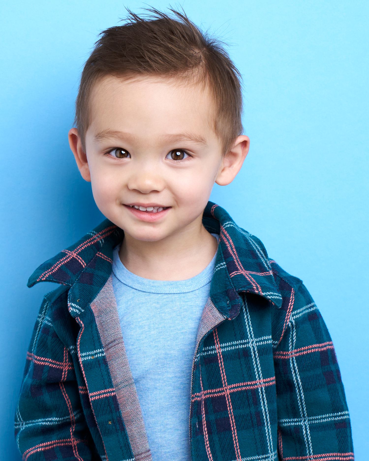 Child in plaid jacket and blue shirt smiling against blue background.