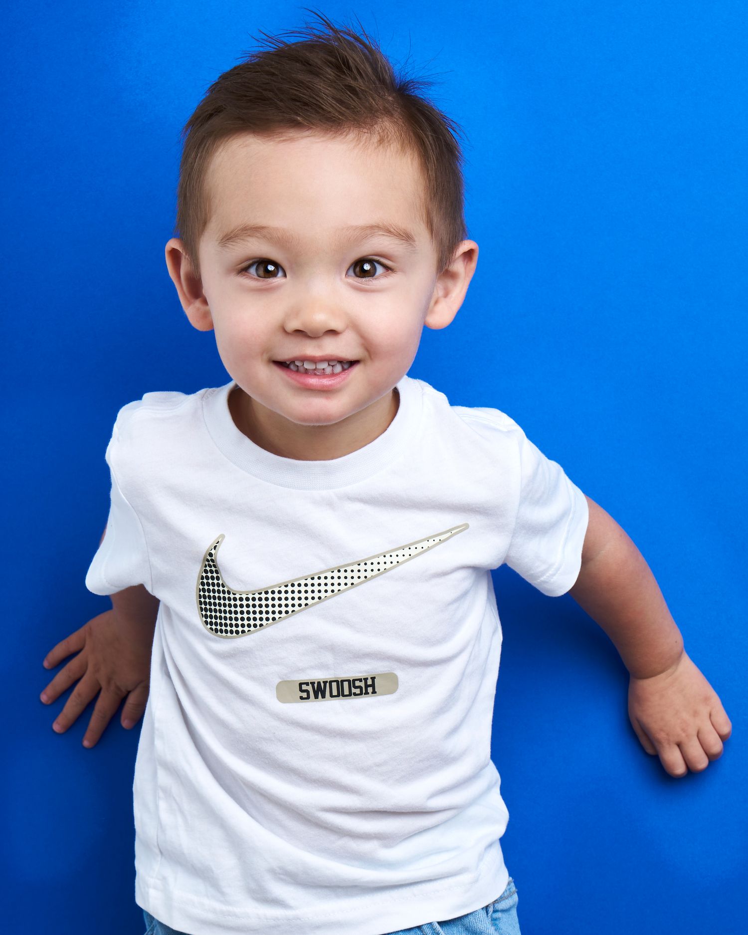 Child wearing white Nike t-shirt posing against bright blue background.