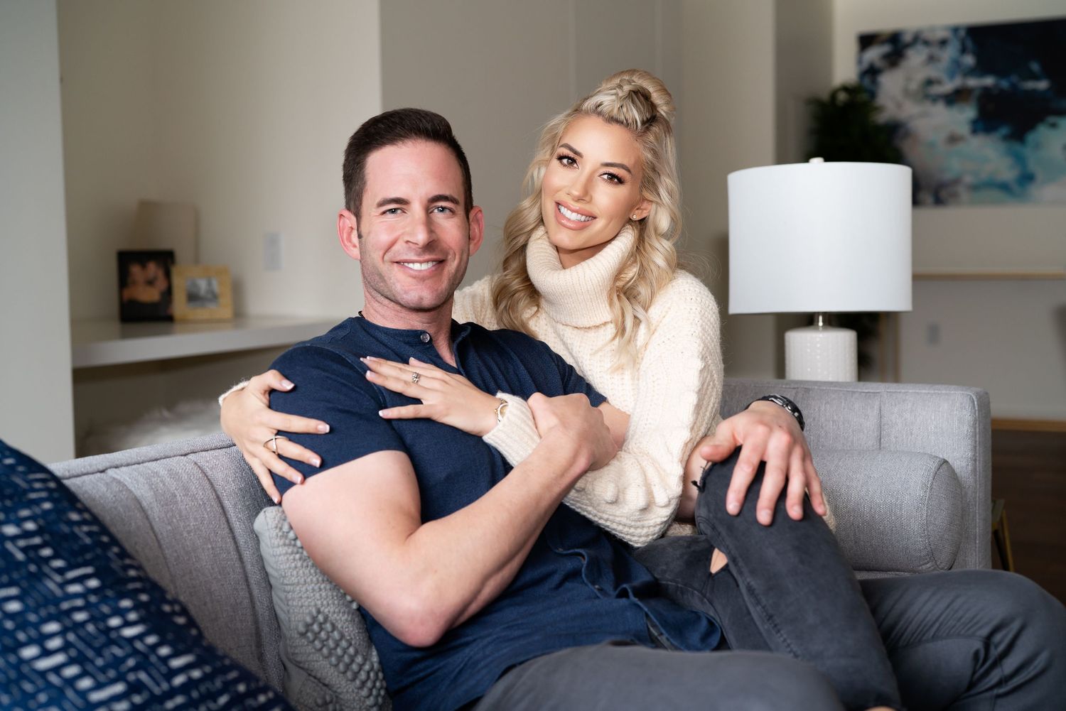 Tarek El Moussa and Heather Rae El Moussa lounging together on a modern sofa in a bright interior for an US Weekly spread.