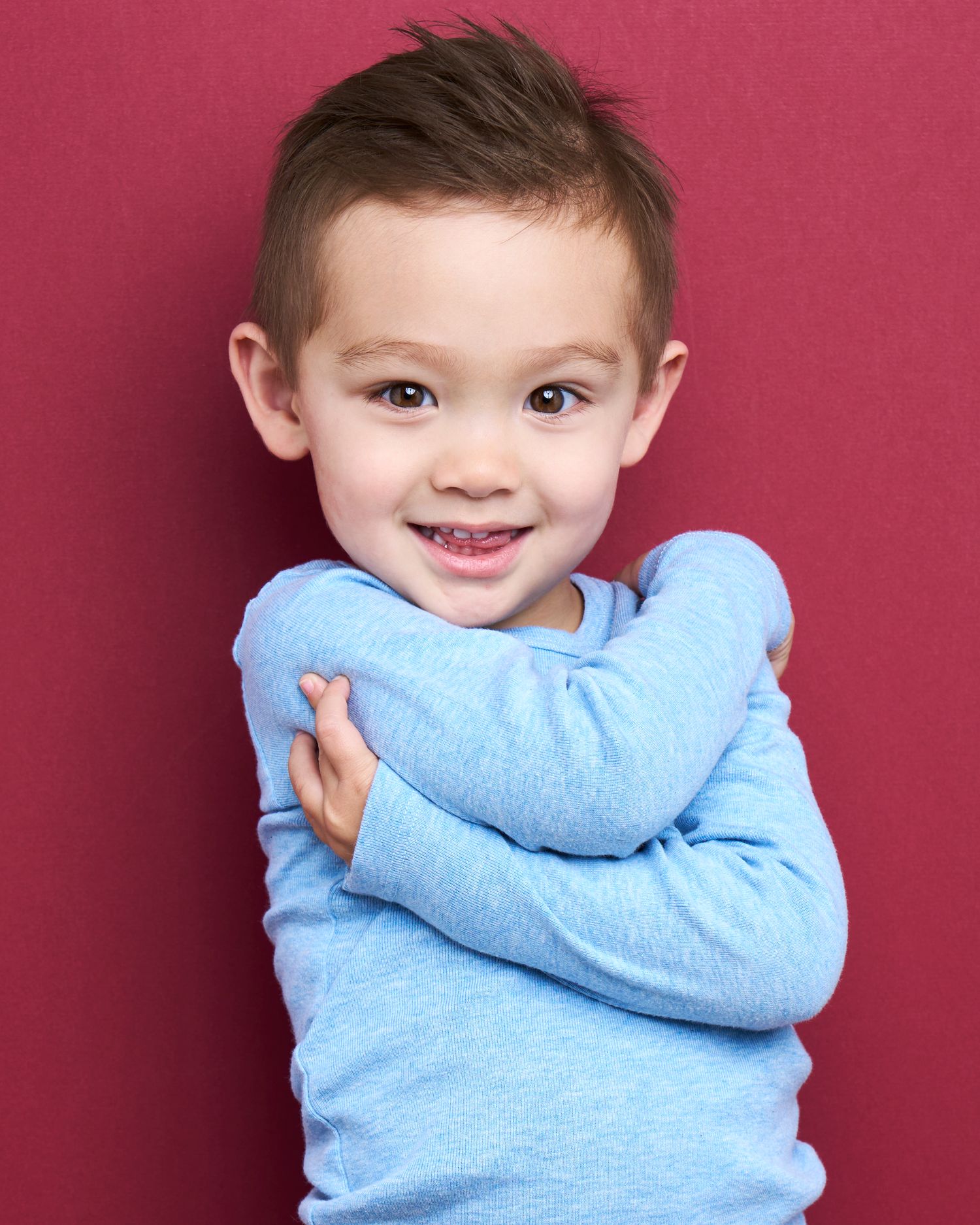 Child wearing light blue sweater making expressive poses against red background.