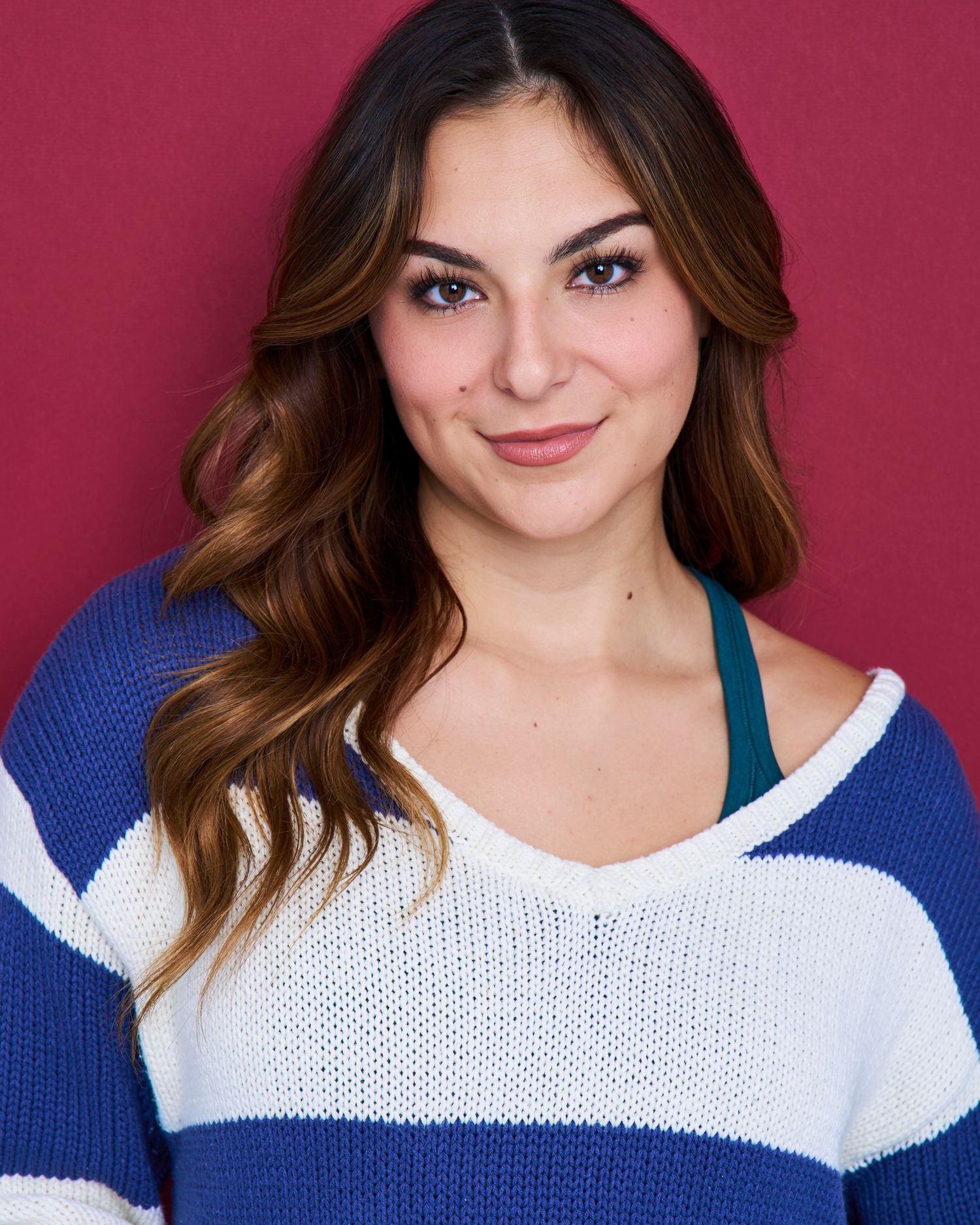 Studio portraits against pink backdrop wearing casual blue and white knit sweater.
