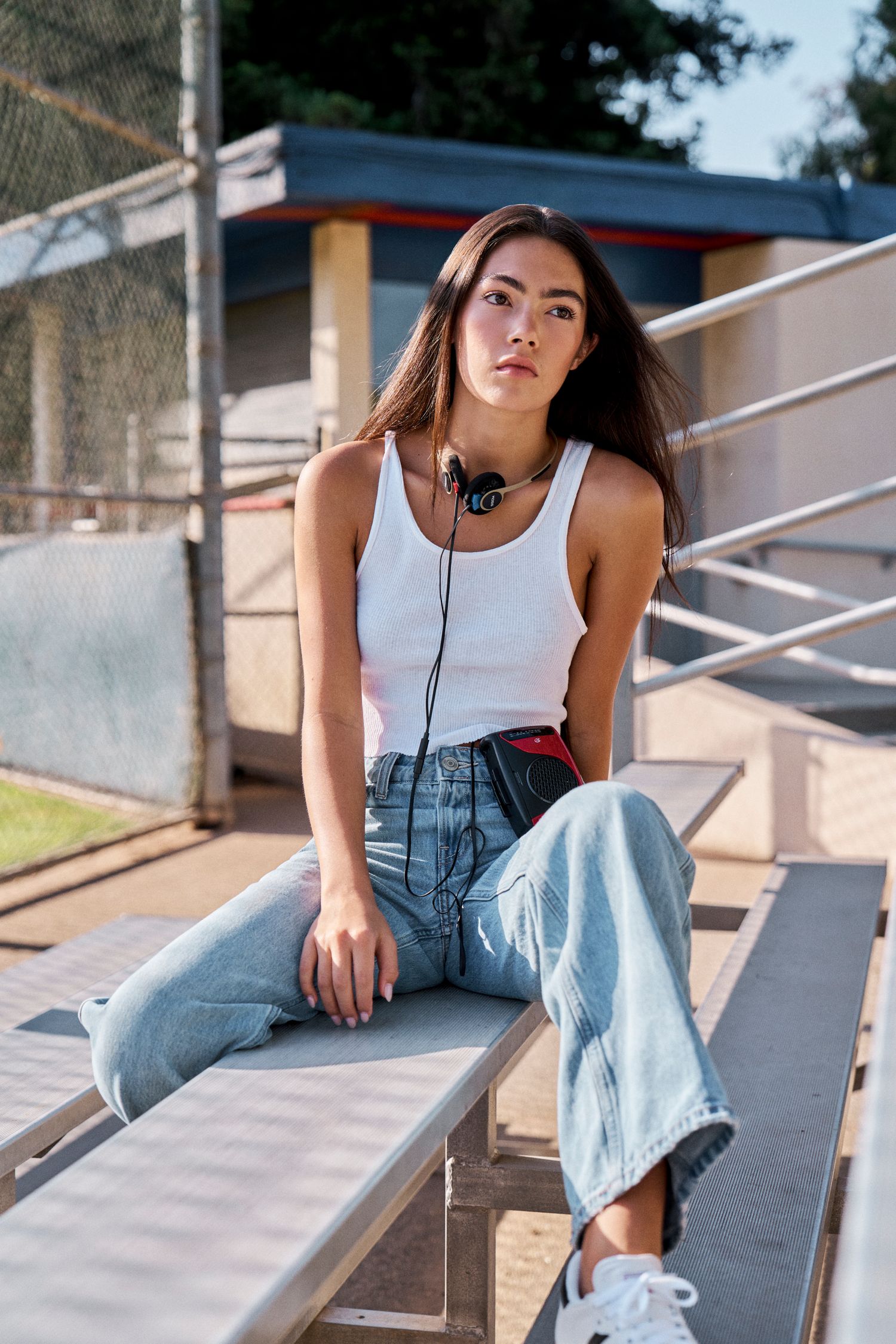 Urban fashion portrait on bleachers wearing tank top and vintage jeans.
