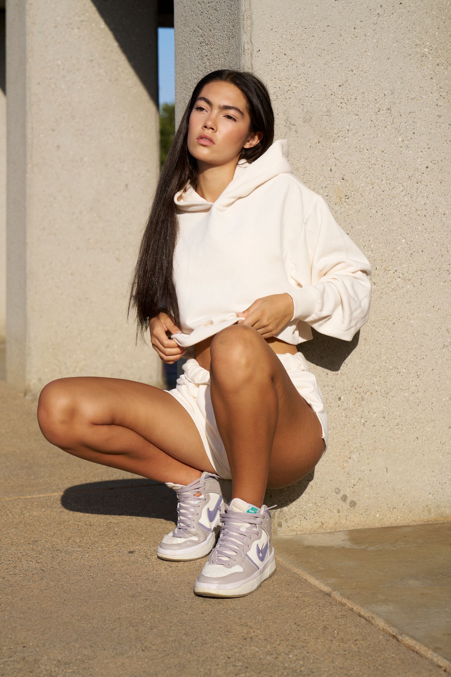 Urban sportswear look with white hoodie and sneakers in architectural setting.