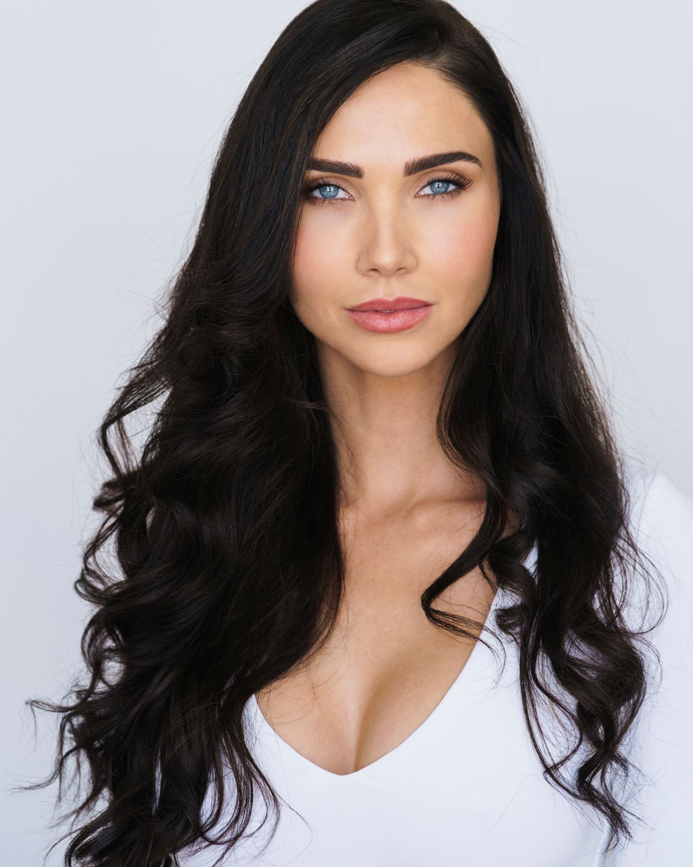Glamour portraits featuring dark wavy hair and natural makeup against white backdrop.