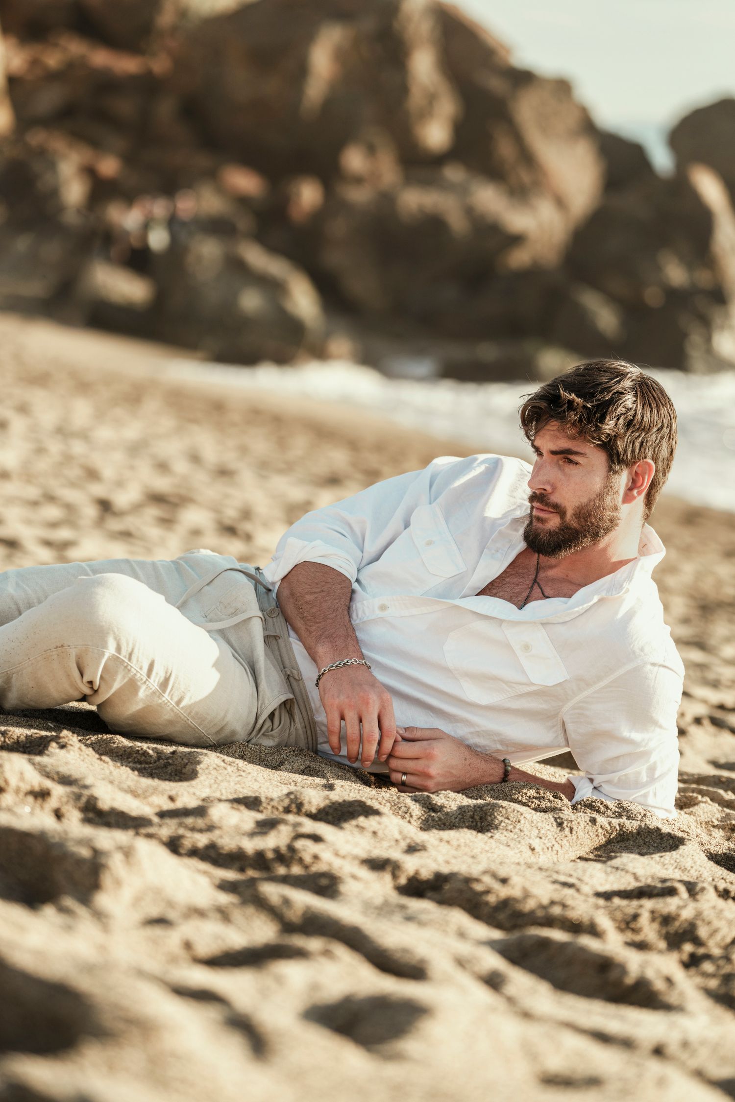 Person in white clothing relaxing on sandy beach during golden hour photography session.