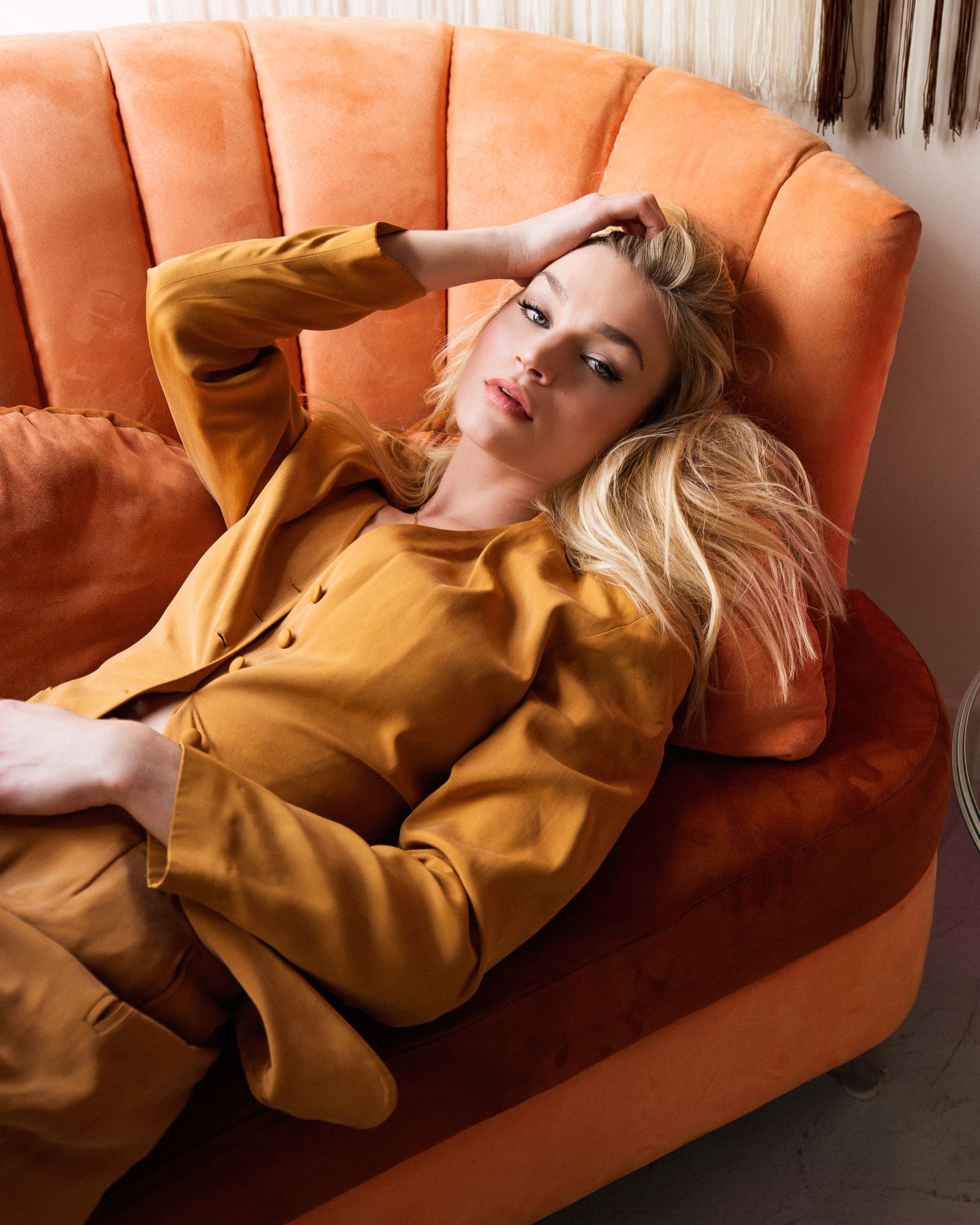 Fashion portrait in mustard blazer lounging on orange velvet sofa.