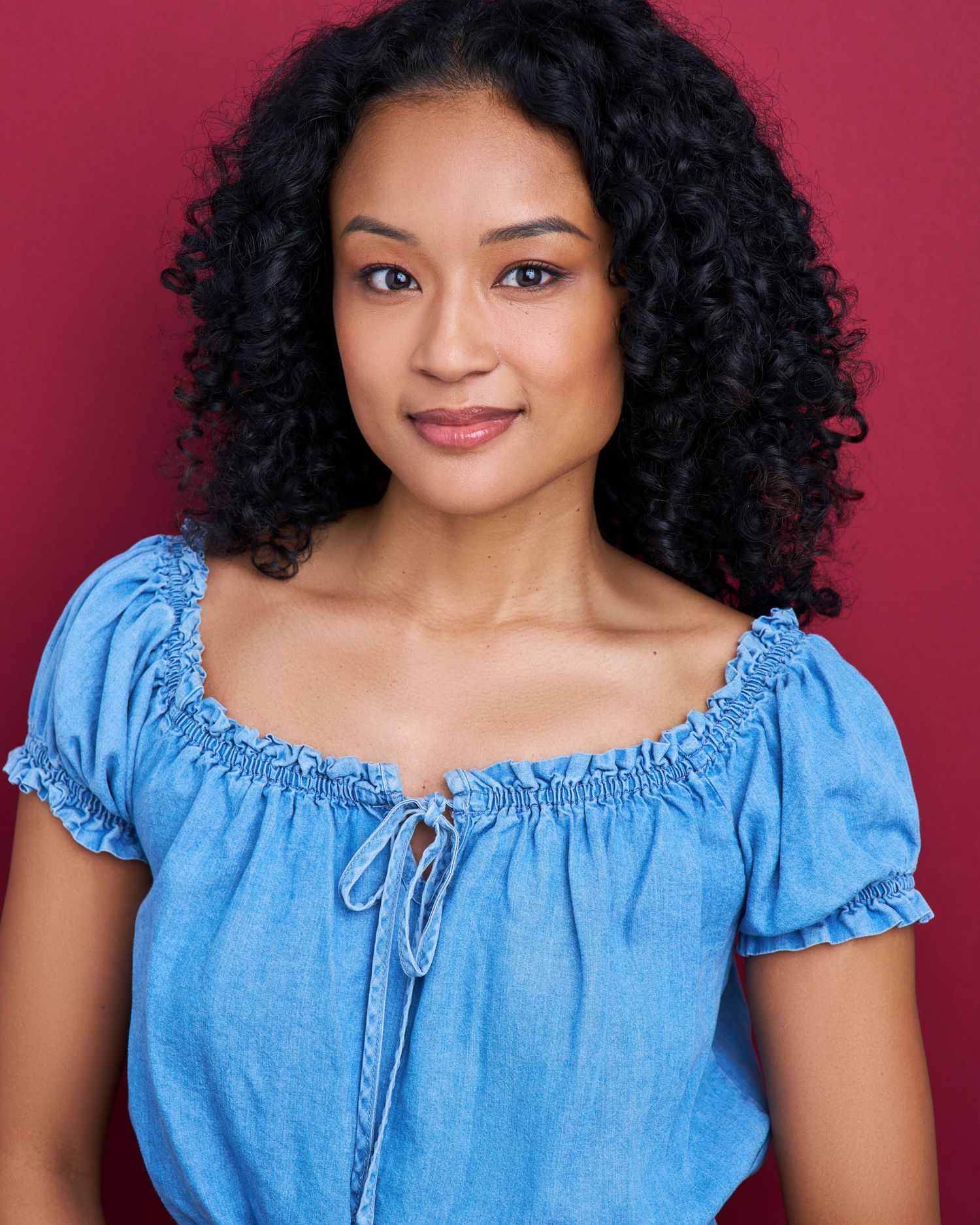 Portrait in light blue peasant top with ruffled sleeves against burgundy background.