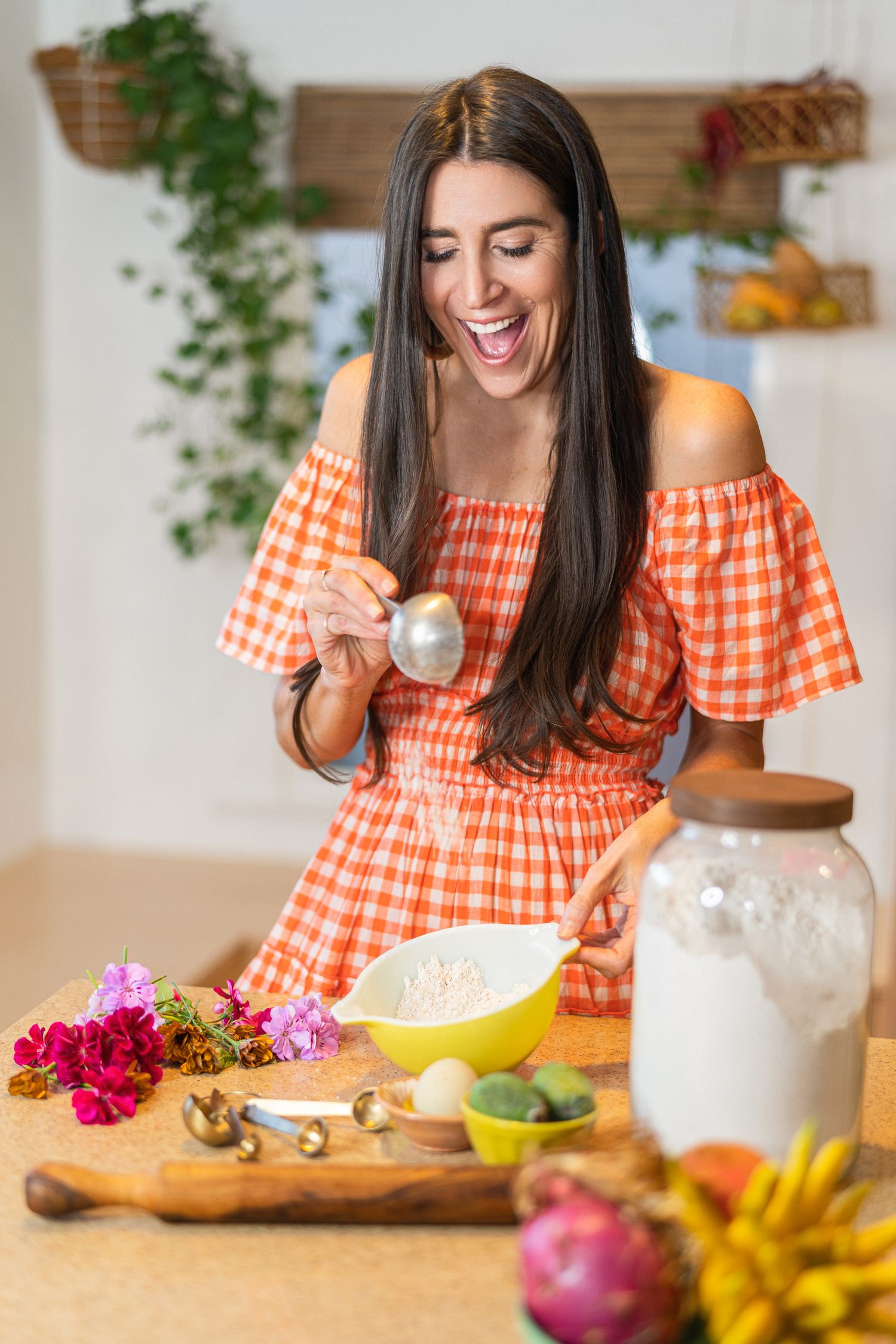 Person in orange dress chopping ingredients with fresh produce and flowers on counter.