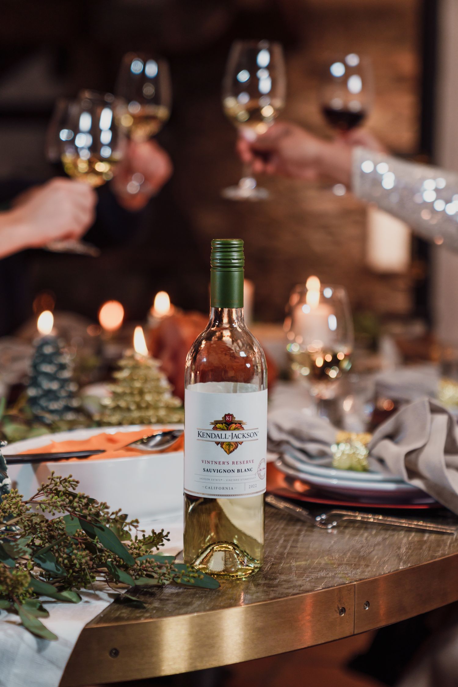 Elegant holiday table setting with wine bottles, candles and evergreen decorations.