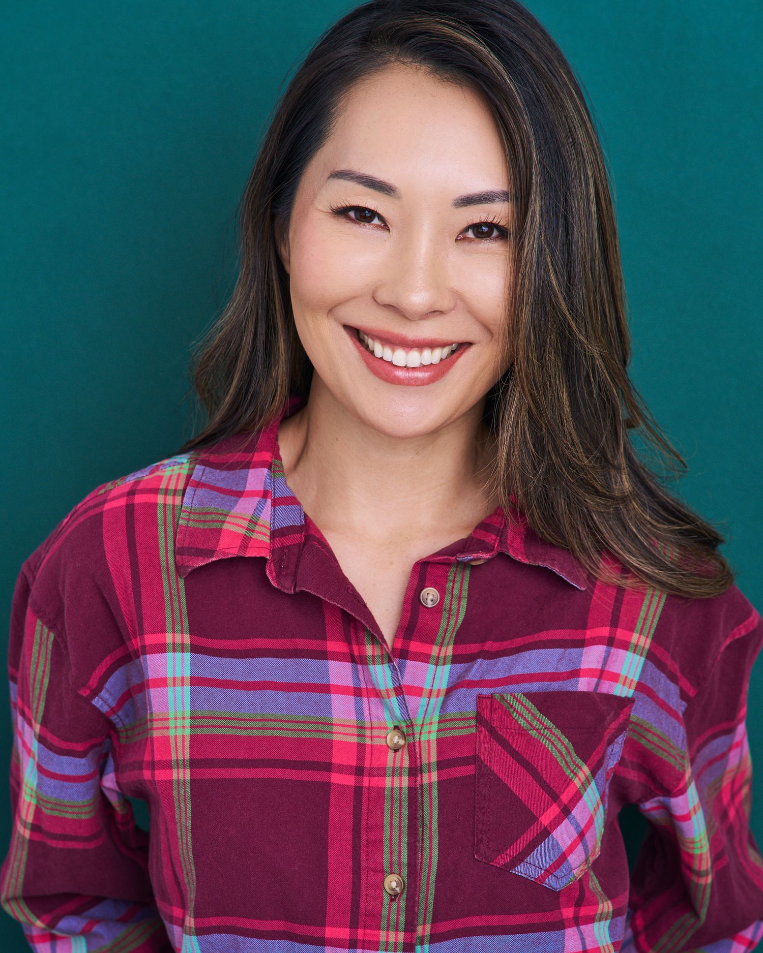 Lifestyle portraits in plaid burgundy shirt showing warm expressions against teal background.