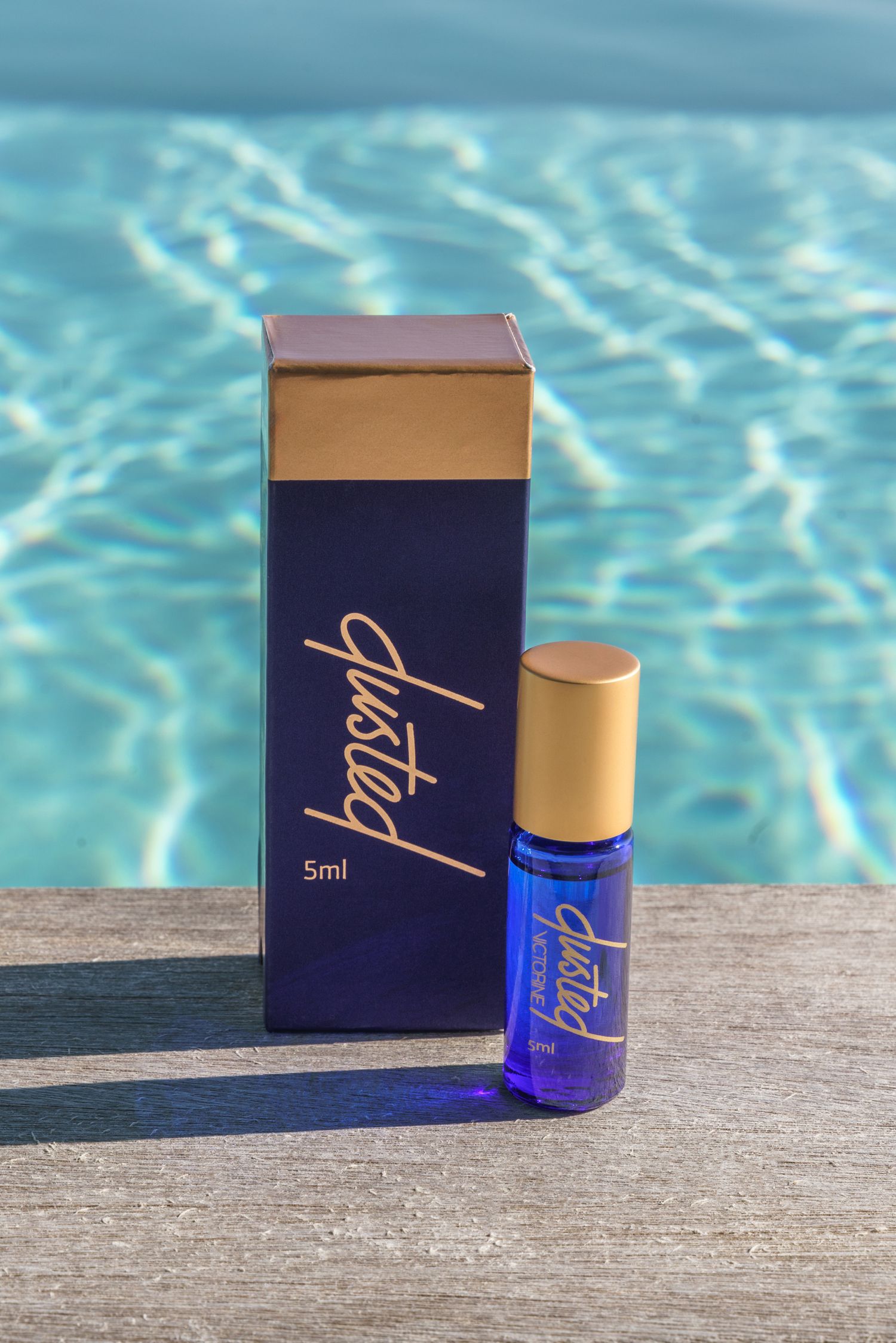 Blue and gold cosmetic product displayed by poolside with reflective water background.