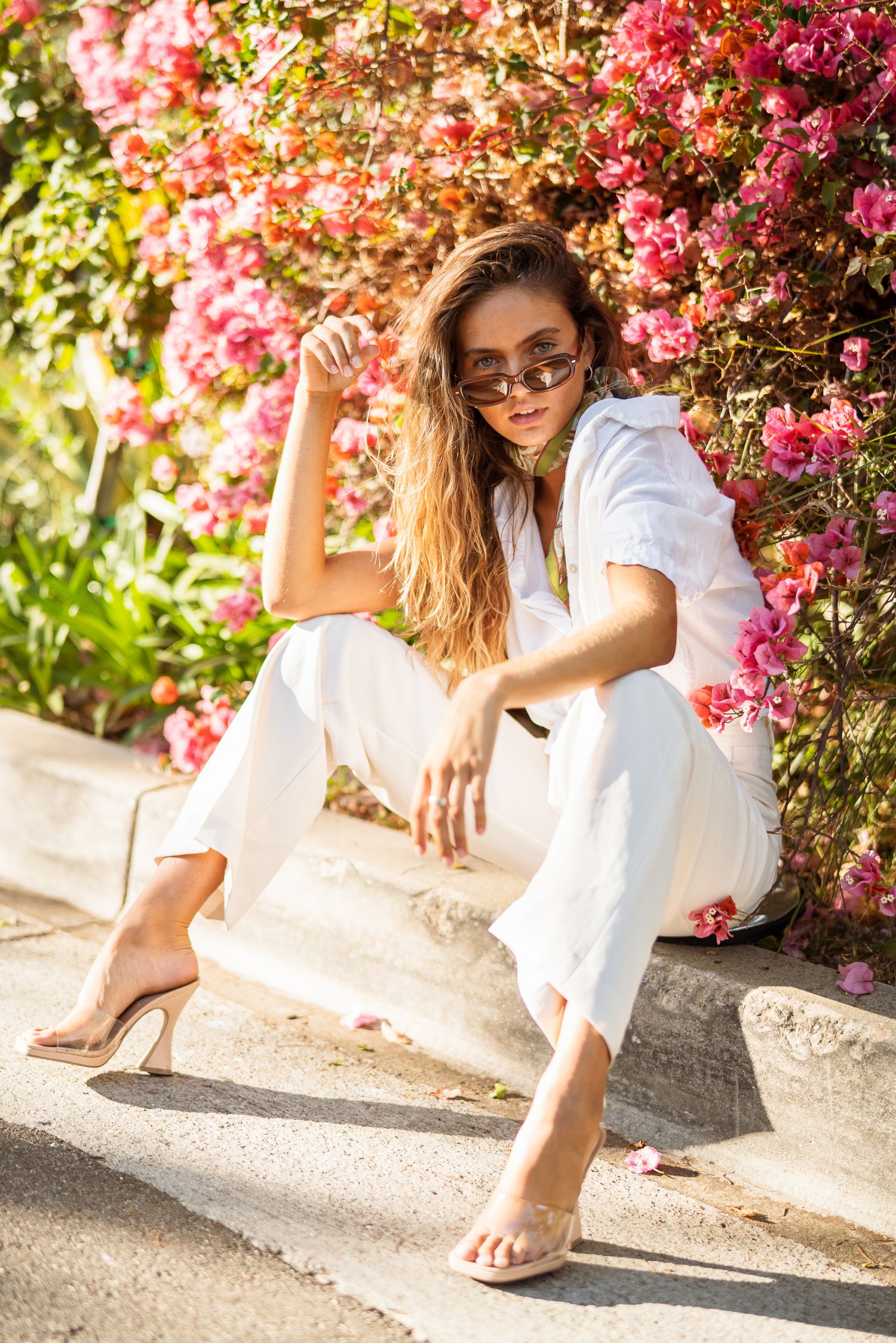 Summer fashion photography with model posing near pink flowering vines in white outfit.