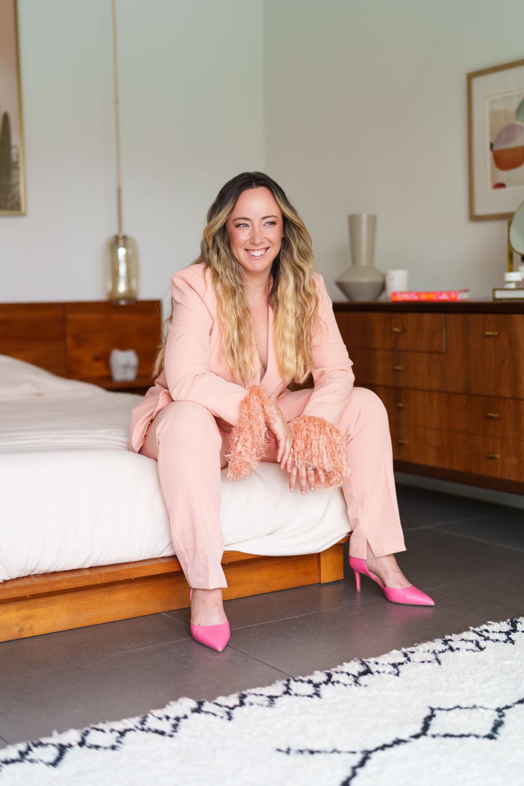 Person in pink outfit reclines on black and white patterned rug in modern room.