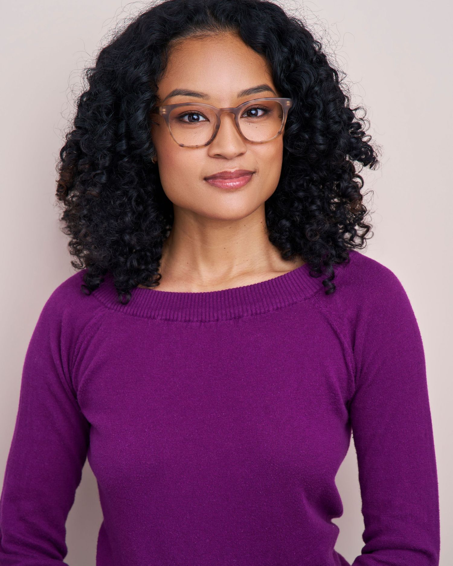 Professional portrait wearing glasses and purple sweater with natural curly hair.
