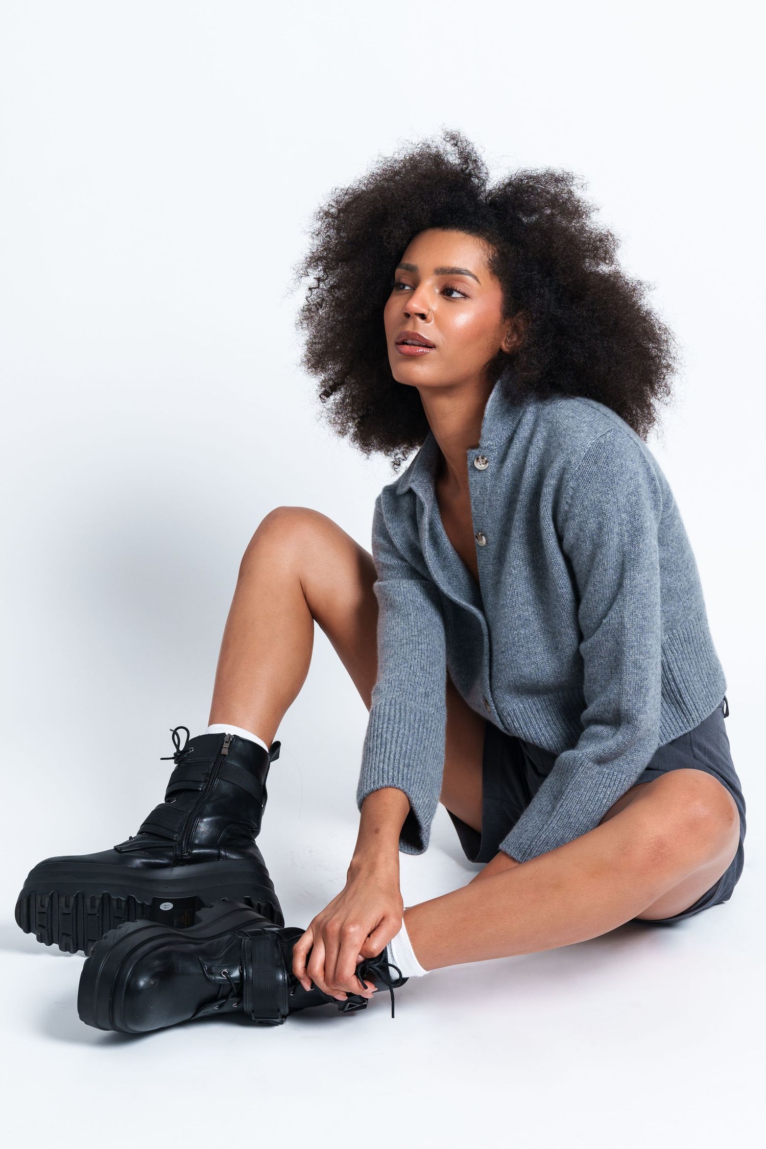 Model showcases gray sweater and black boots in artistic studio poses.