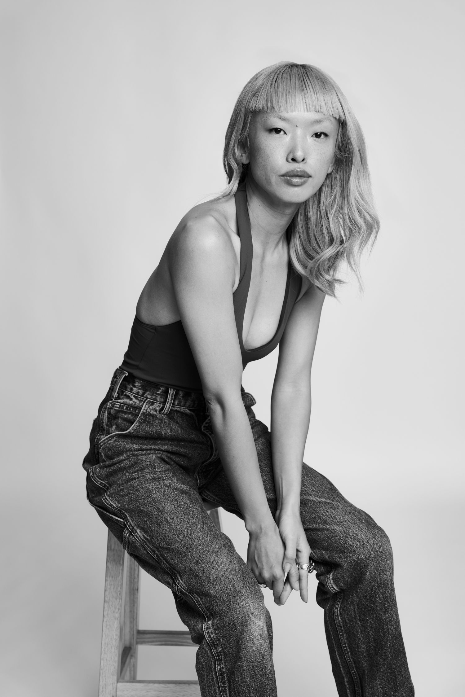 Black and white fashion photoshoot featuring a model in denim jeans and dark tank top against white background.