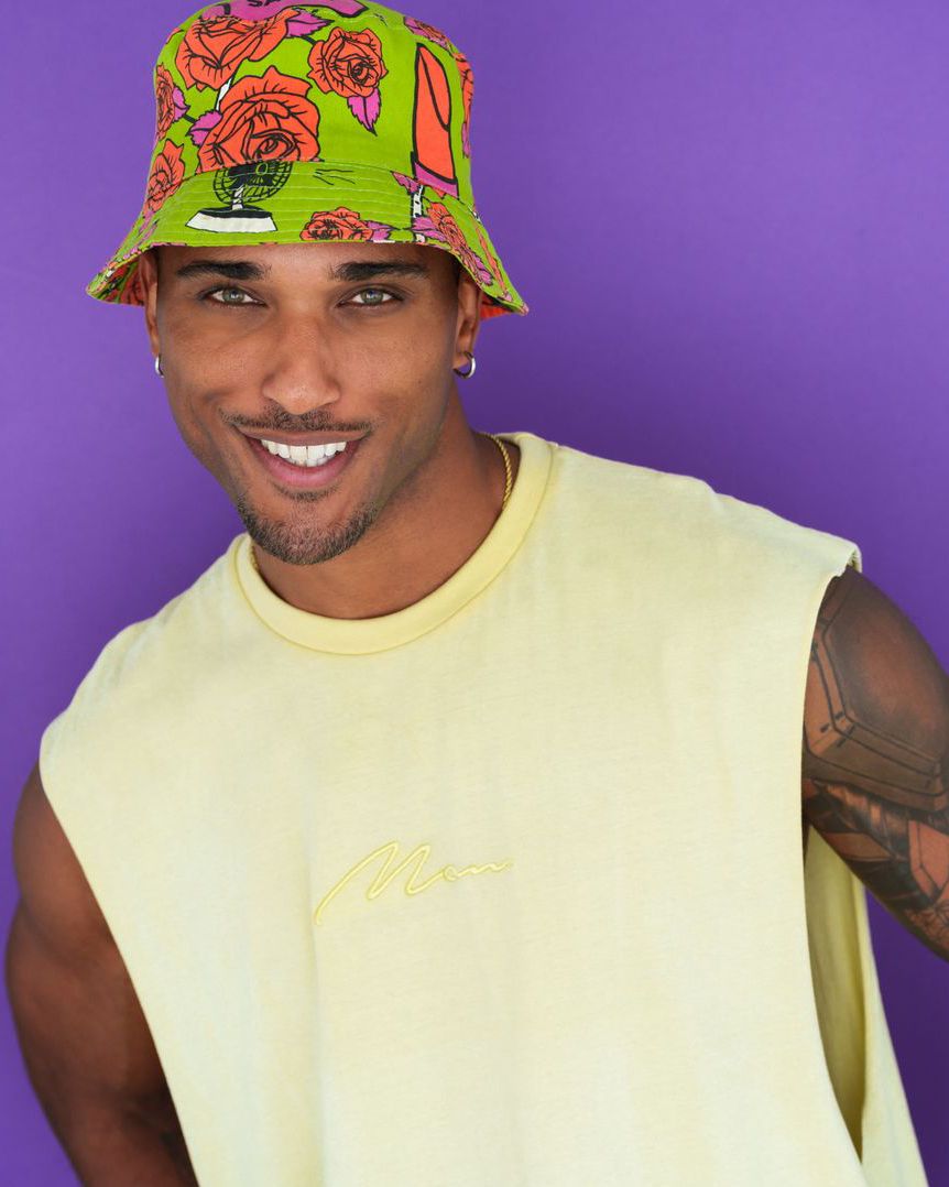Vibrant portraits wearing floral bucket hat and yellow tank top against purple background.