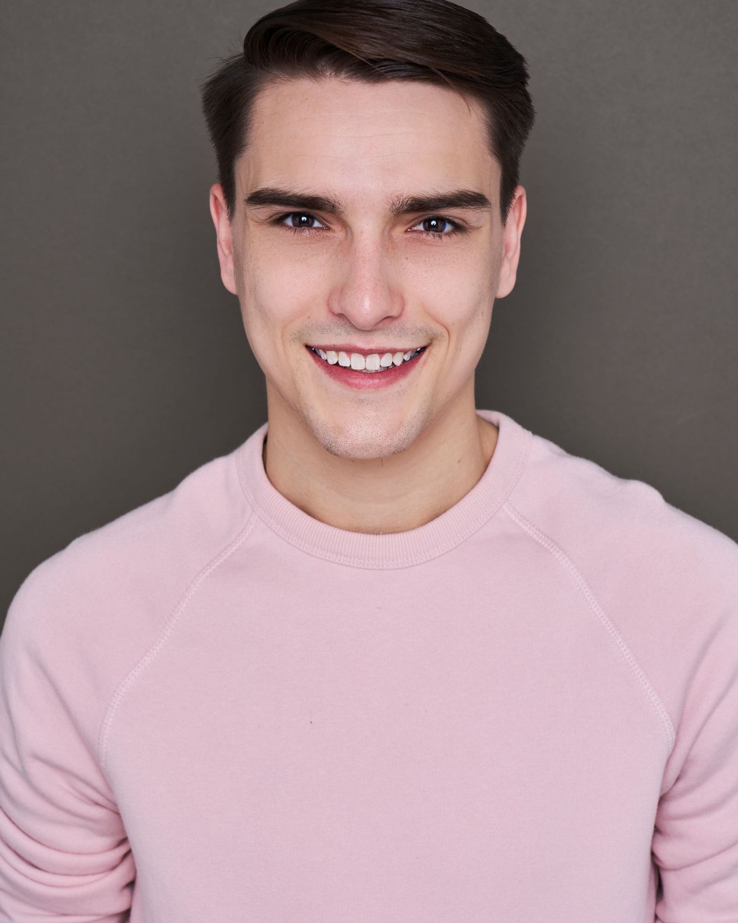 Portrait series featuring warm smiles and expressions while wearing a light pink sweater against grey backdrop.