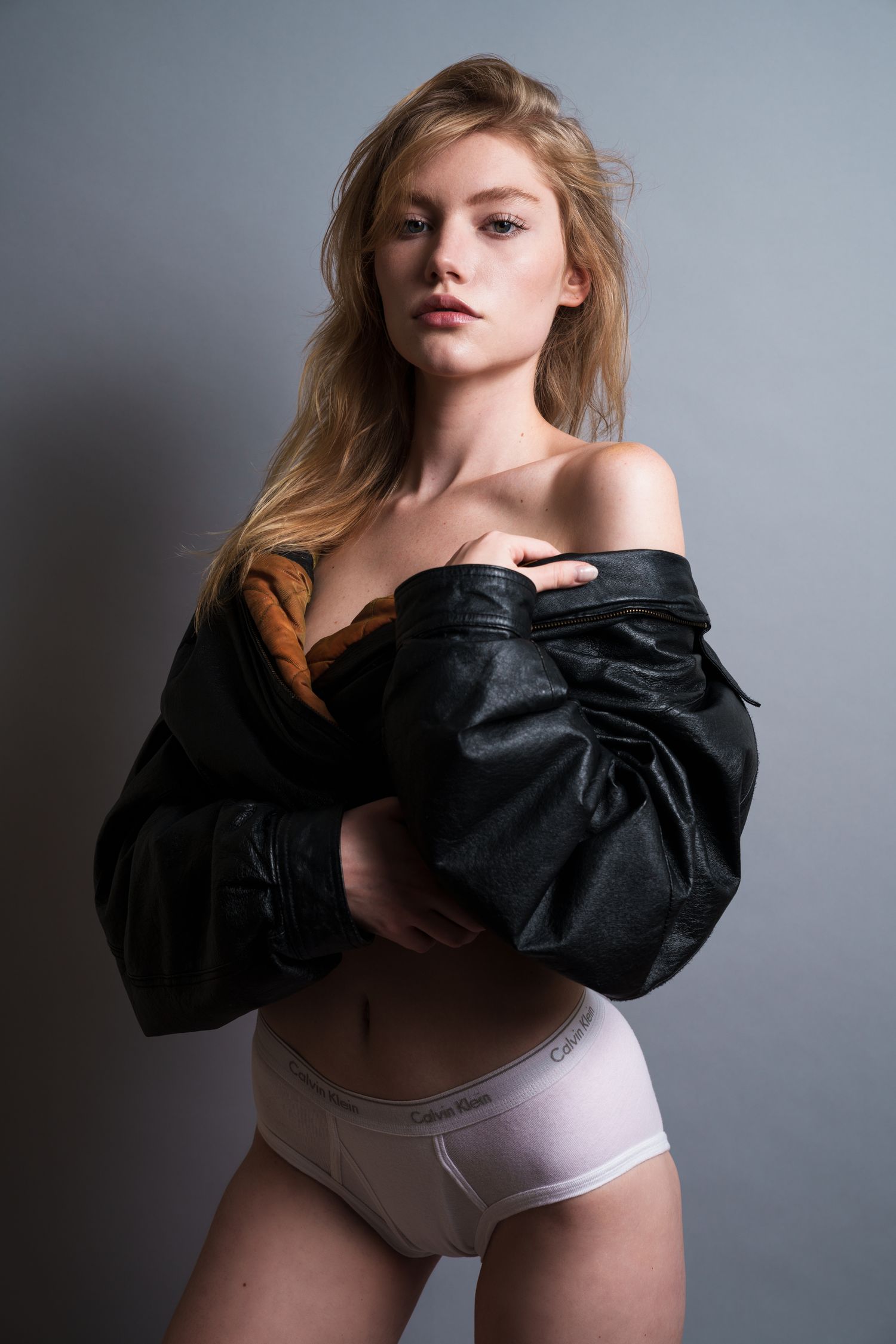 Studio fashion shot of model wearing oversized black jacket and light undergarments.