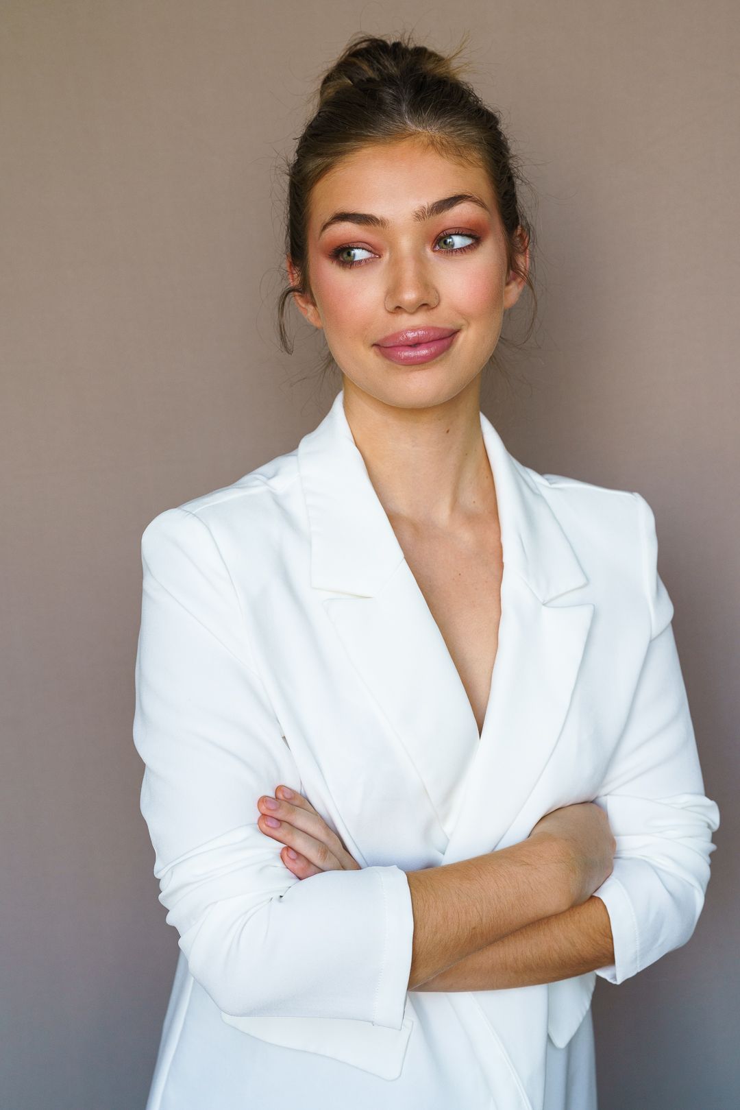 Elegant studio portrait in white blazer with arms crossed.