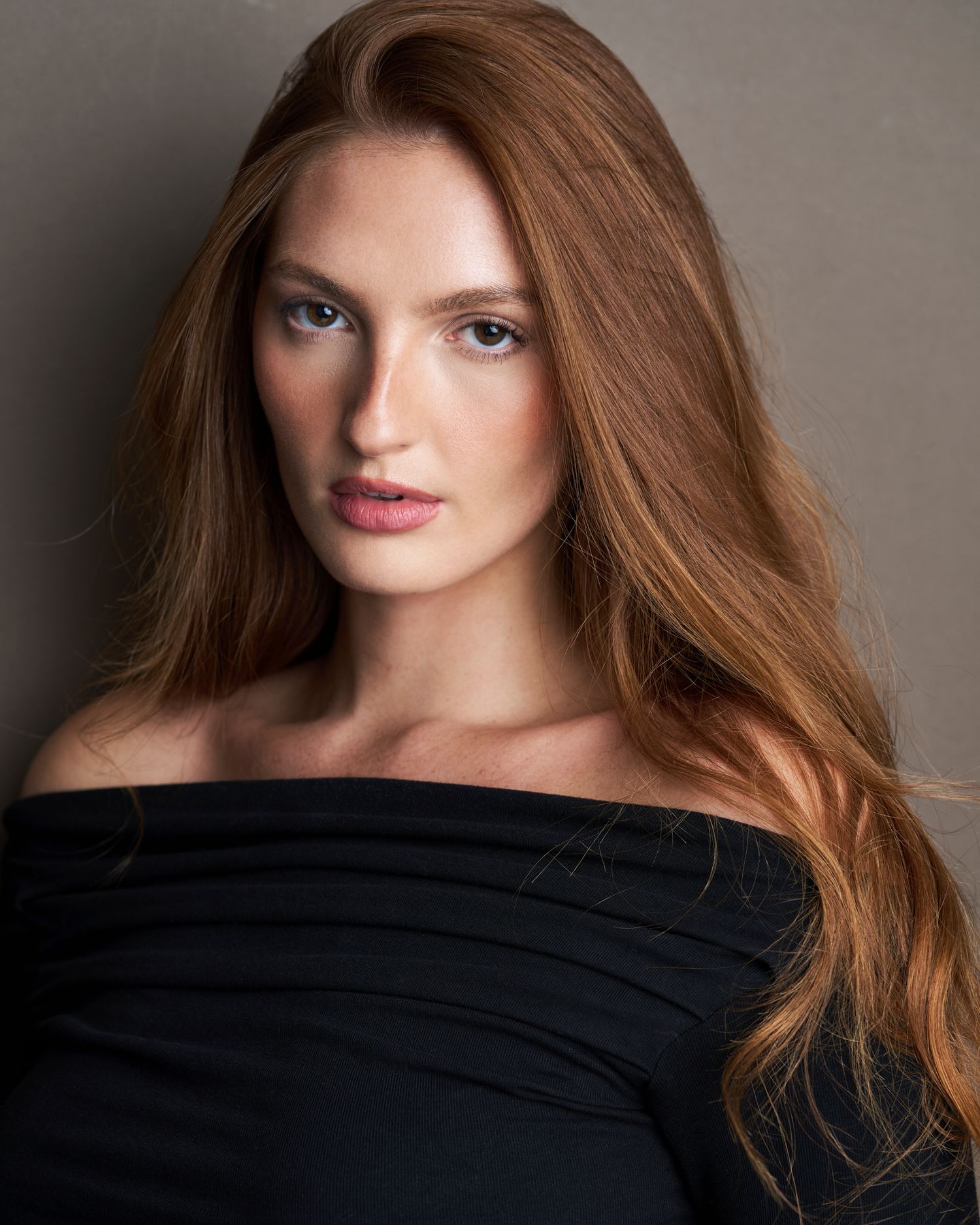 Portrait of woman with long auburn hair against grey background in dramatic lighting.