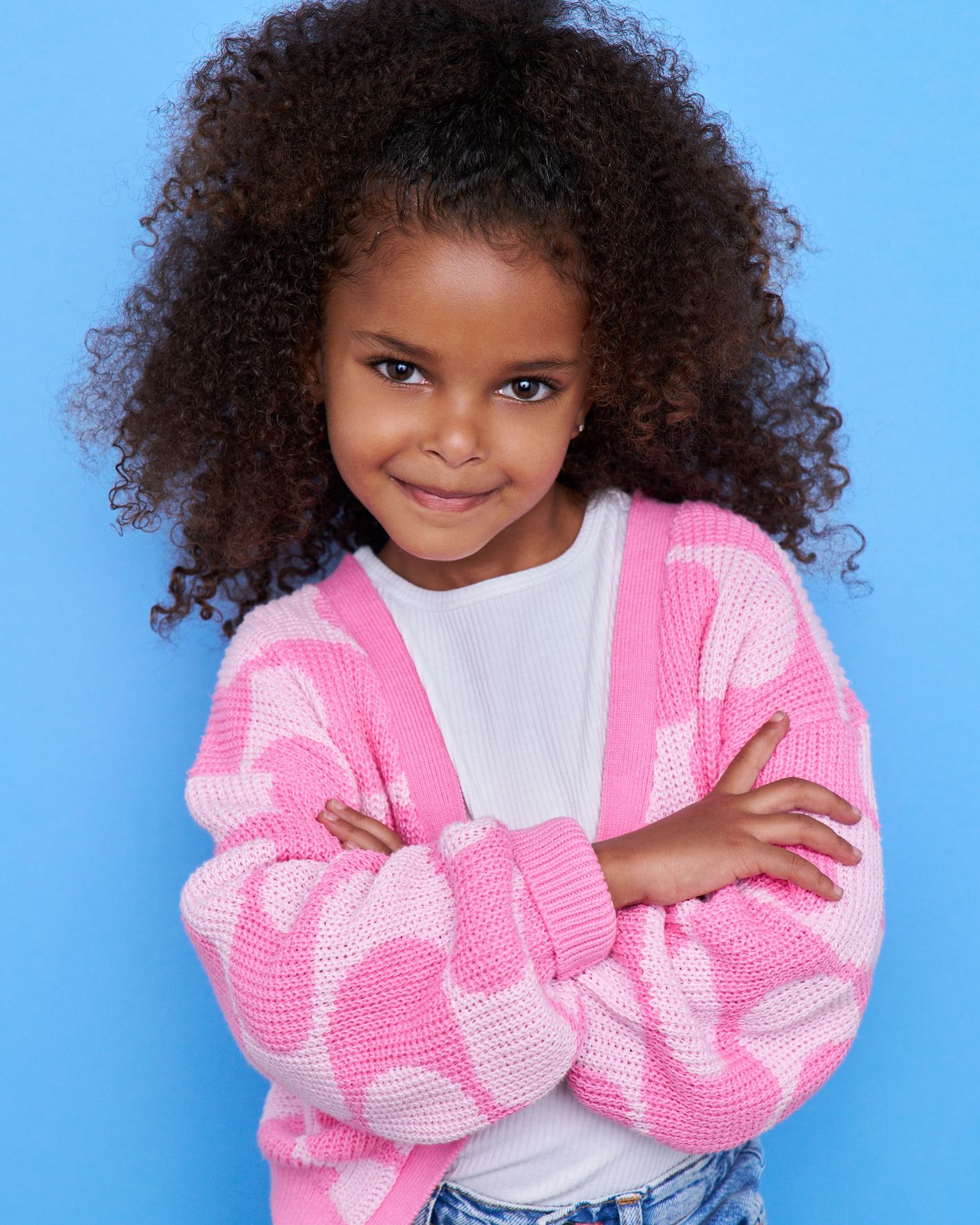 Young portrait in pink and white patterned sweater with natural curly hair.