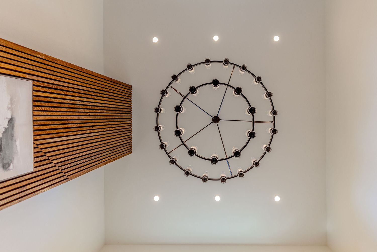 Modern living room features wood slat wall accent, circular pendant lights, and recessed lighting against white walls.