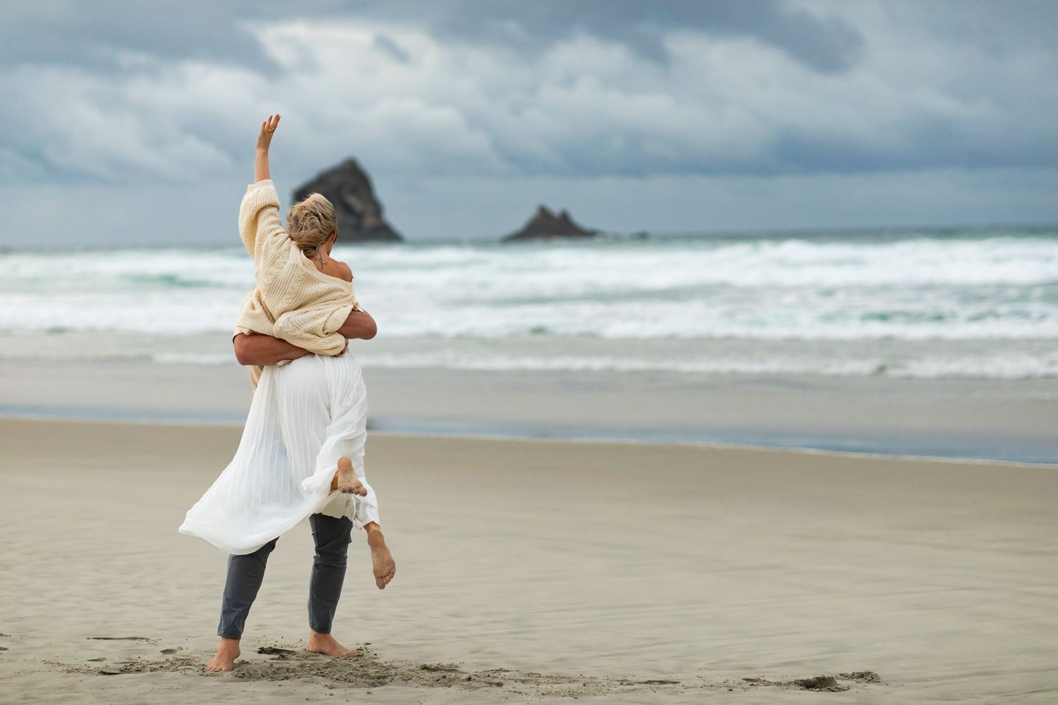 Happy couple dancing together on a scenic beach with waves in the background.