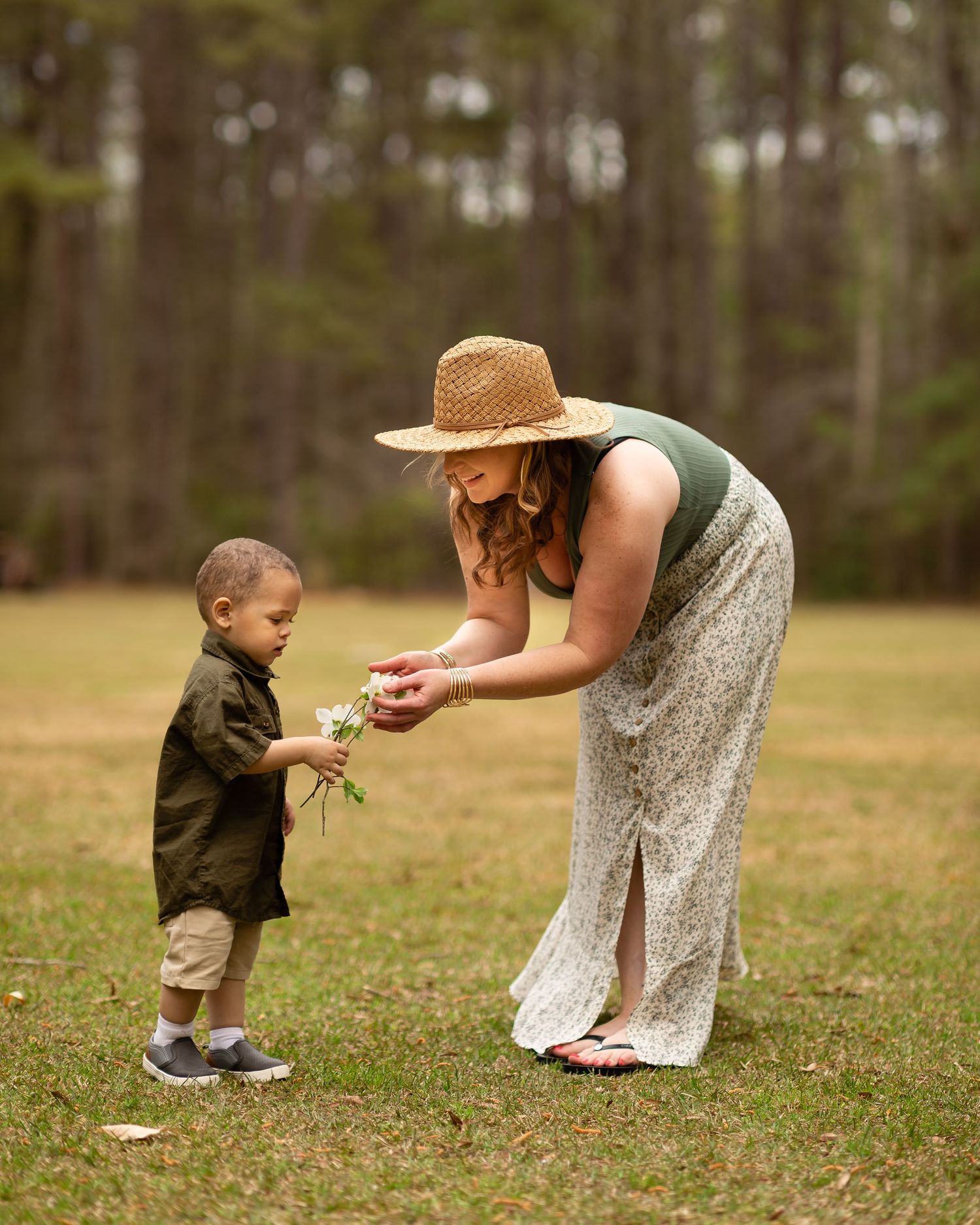 A tender moment in nature as two people share a gentle interaction on a grassy field with trees in the background.