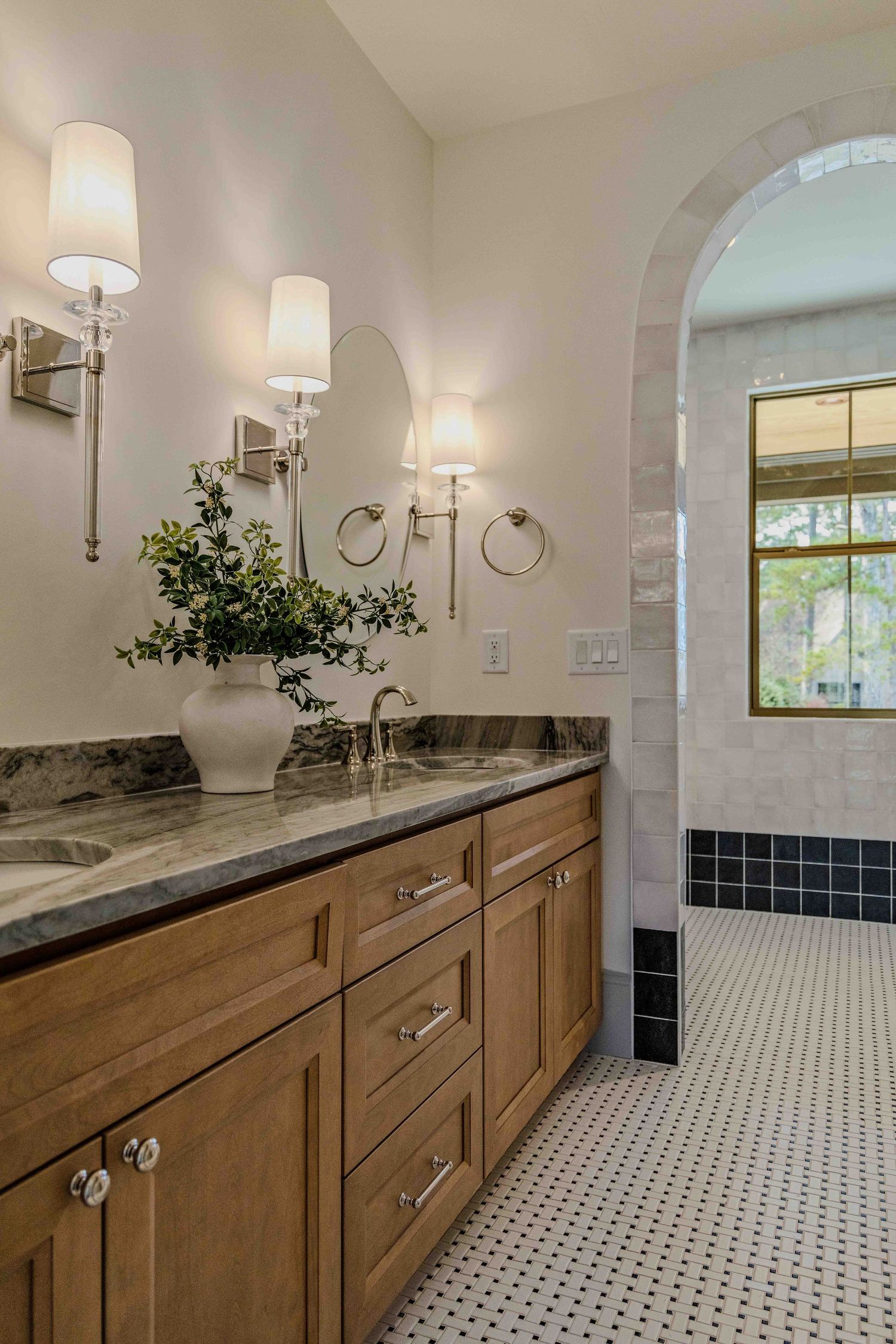 Modern bathroom with wood cabinets, black and white mosaic floor tiles, and chrome wall sconces creates a timeless design.