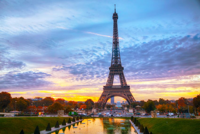Eiffel Tower silhouetted against a dramatic sunset sky with vibrant orange clouds reflected in pools at Trocadero, Paris.