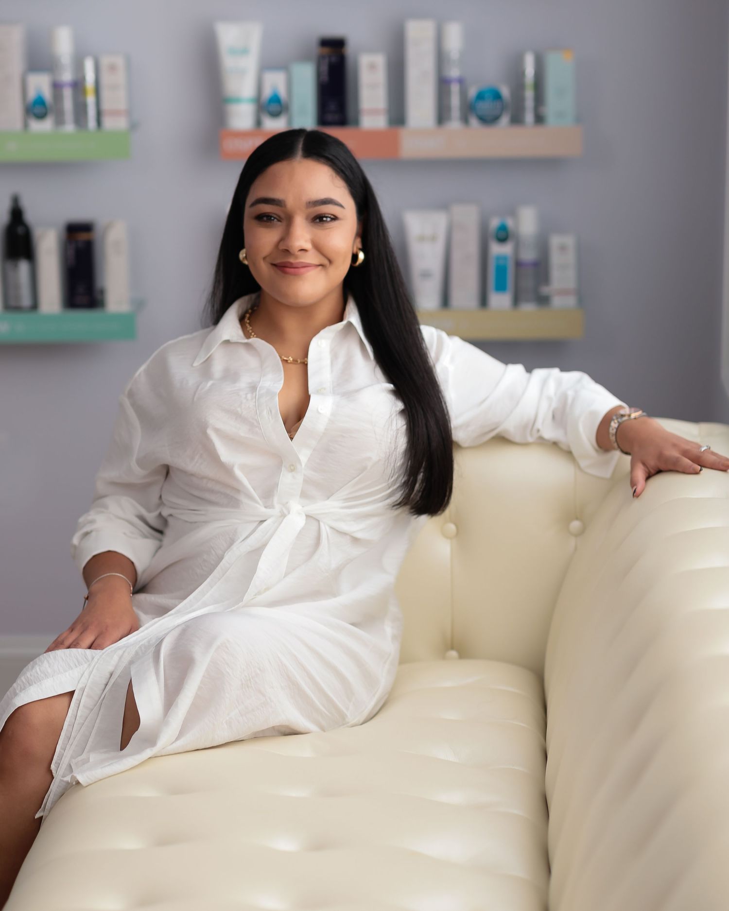 Lifestyle portrait in white dress shirt on cream couch with beauty products displayed.
