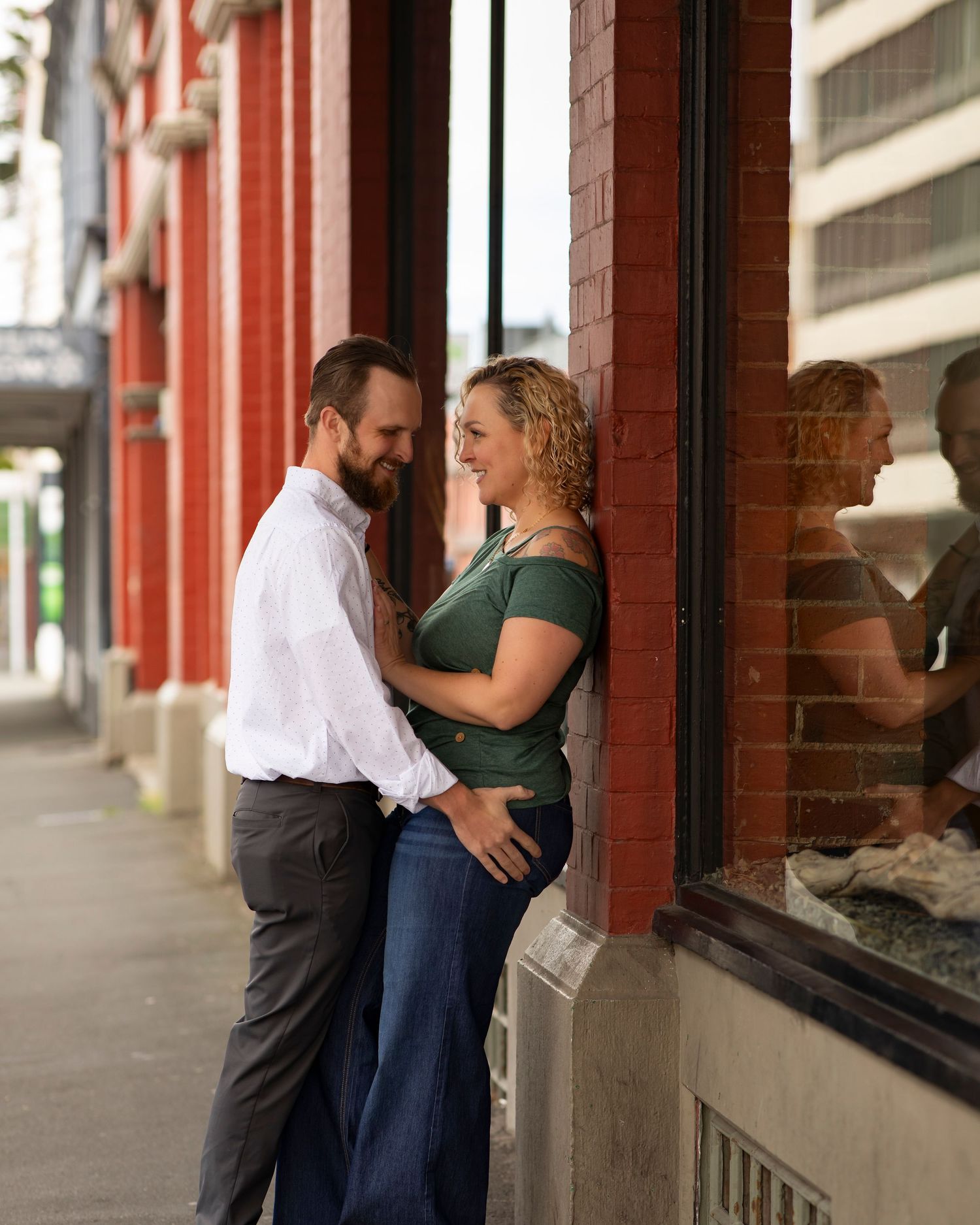A couple embraces intimately while standing under a covered walkway with red pillars and storefronts.