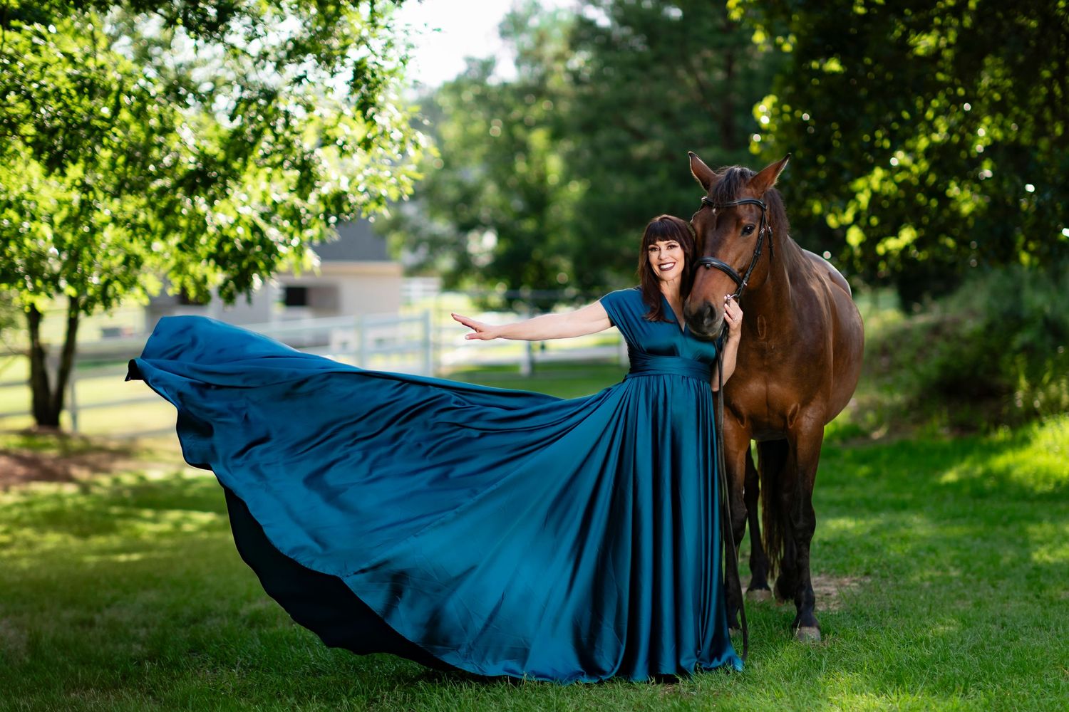 Dramatic portrait of a flowing blue ballgown dress alongside a majestic brown horse in a sunlit garden setting.
