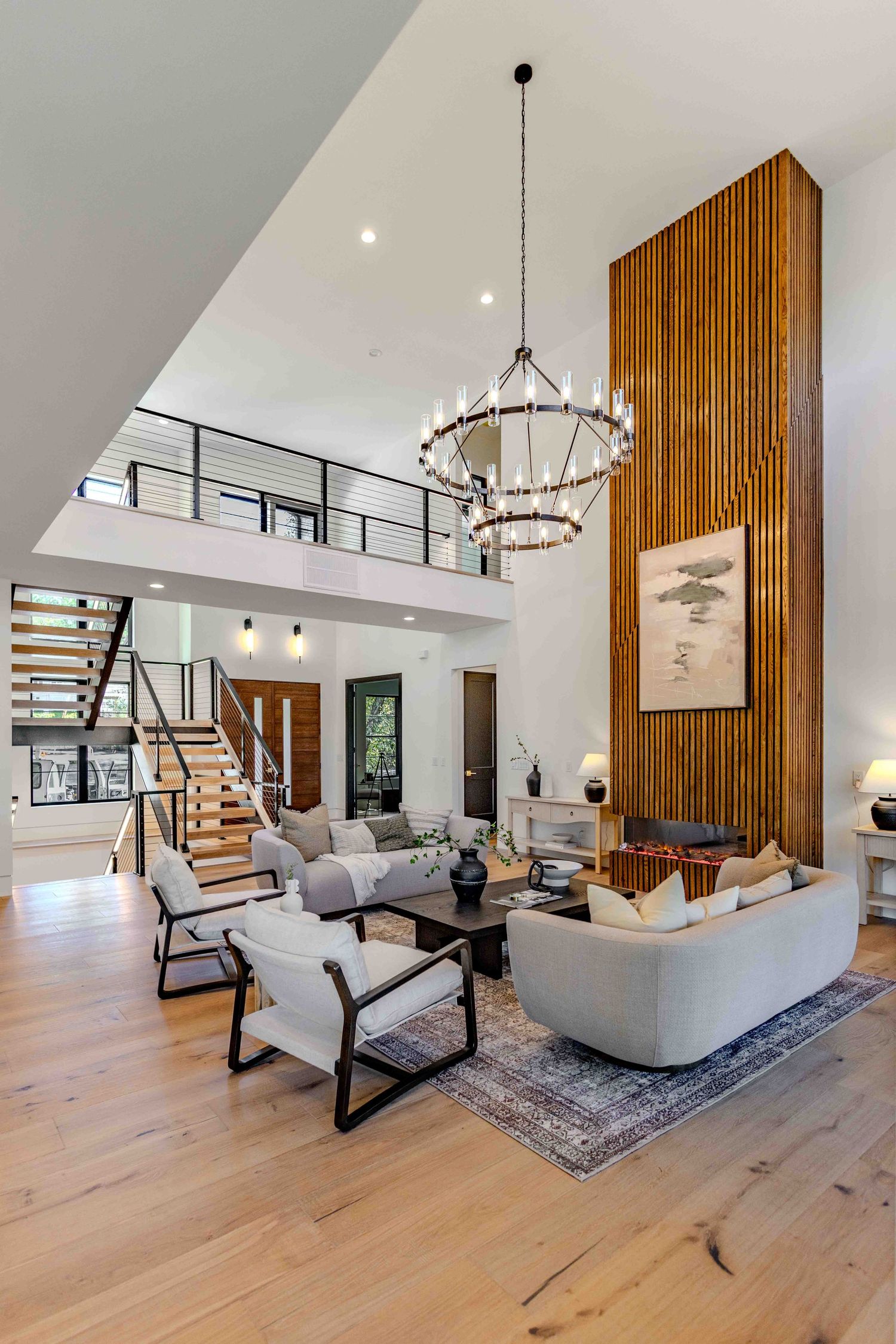 Modern living room with wood accent wall, circular chandelier, grey sofa, and light hardwood flooring.
