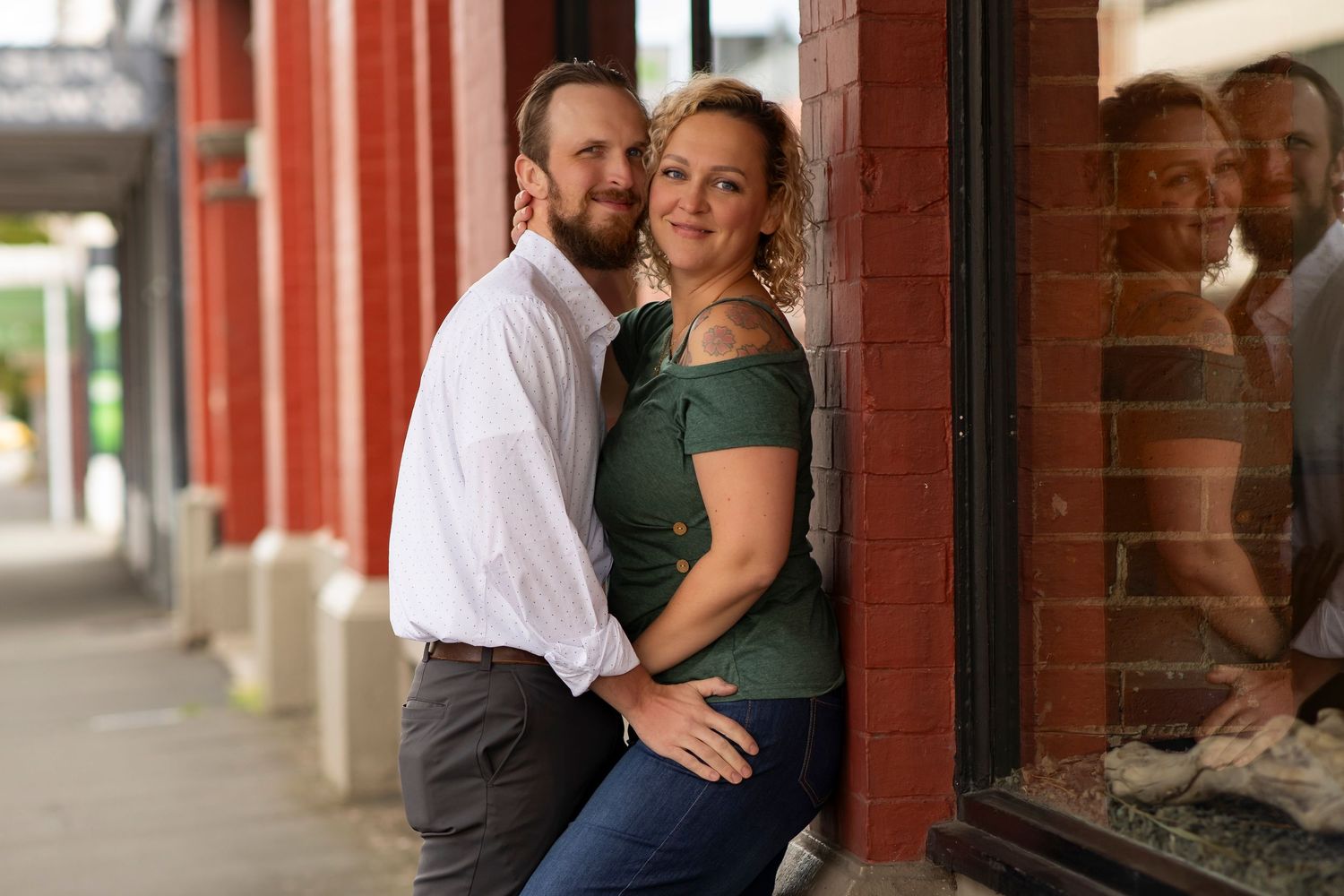A couple in casual attire shares an intimate moment while standing in a covered walkway with brick columns.