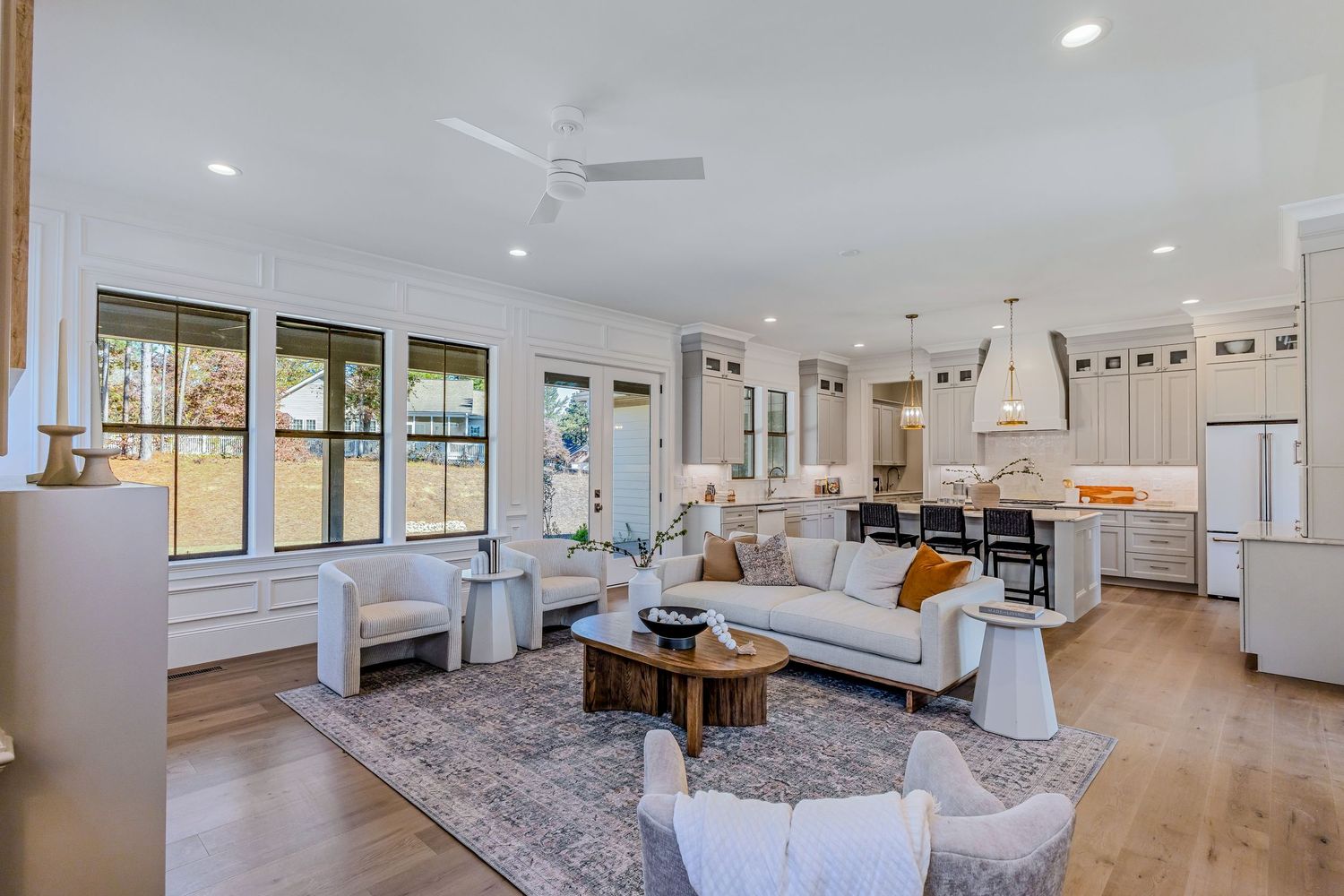 Modern open concept living room with hardwood floors, white walls, and large windows letting in natural light.