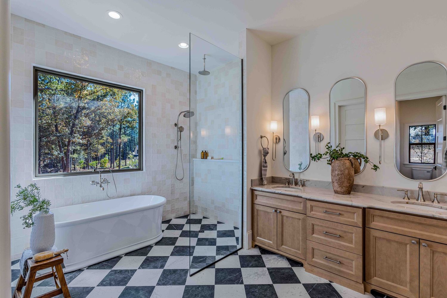 Modern bathroom interior with black and white checkered floor tiles and light wood vanity featuring elegant wall sconces.