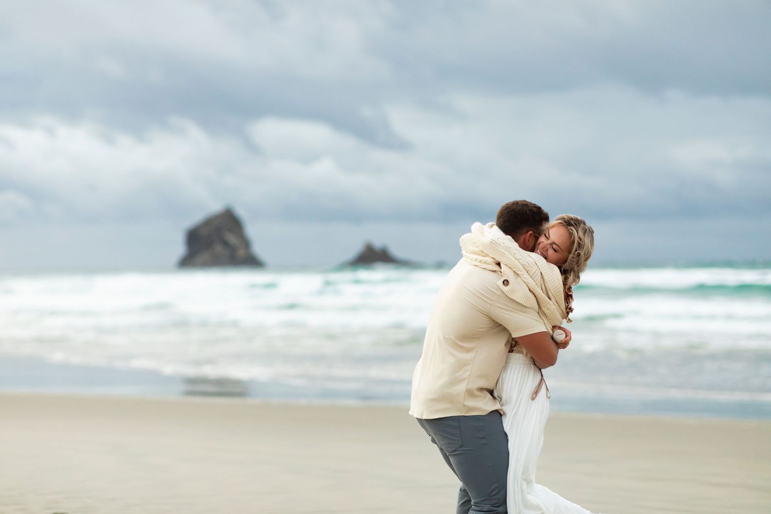 Romantic embrace on a moody beach with dramatic rock formations in the distance.