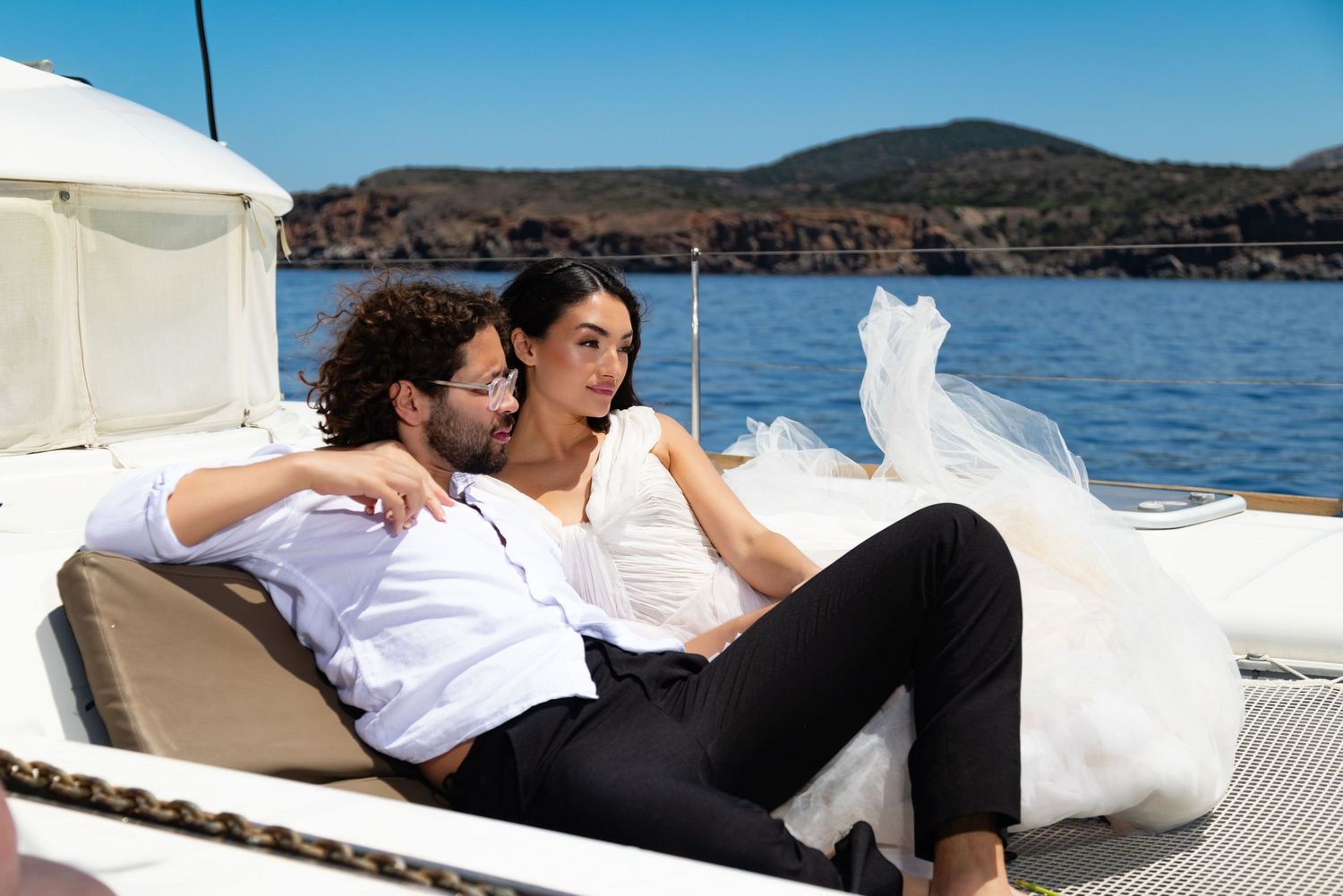 A couple lounges together on a yacht enjoying a scenic ocean view on a sunny afternoon.