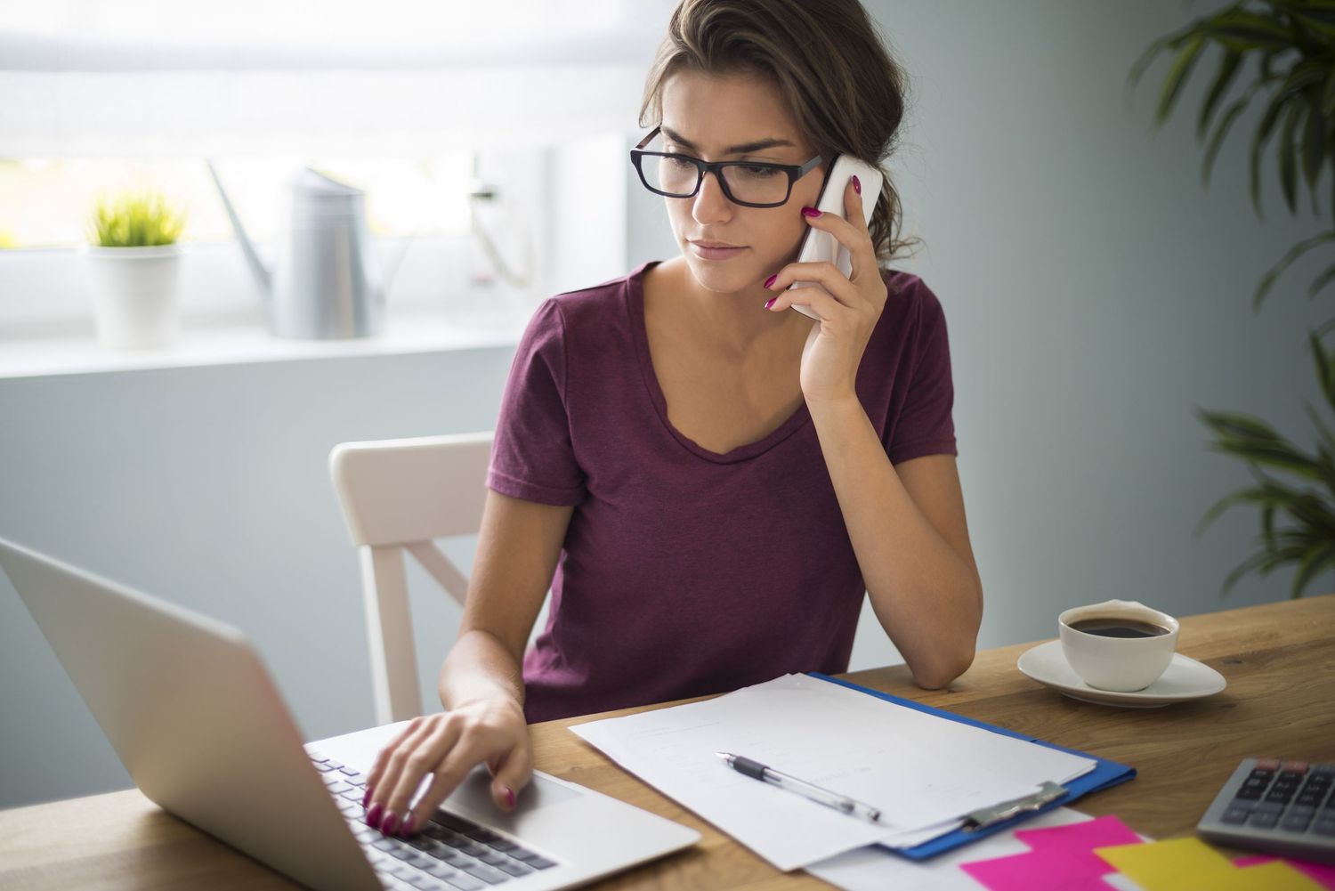 A person working from home office while talking on phone and using laptop.