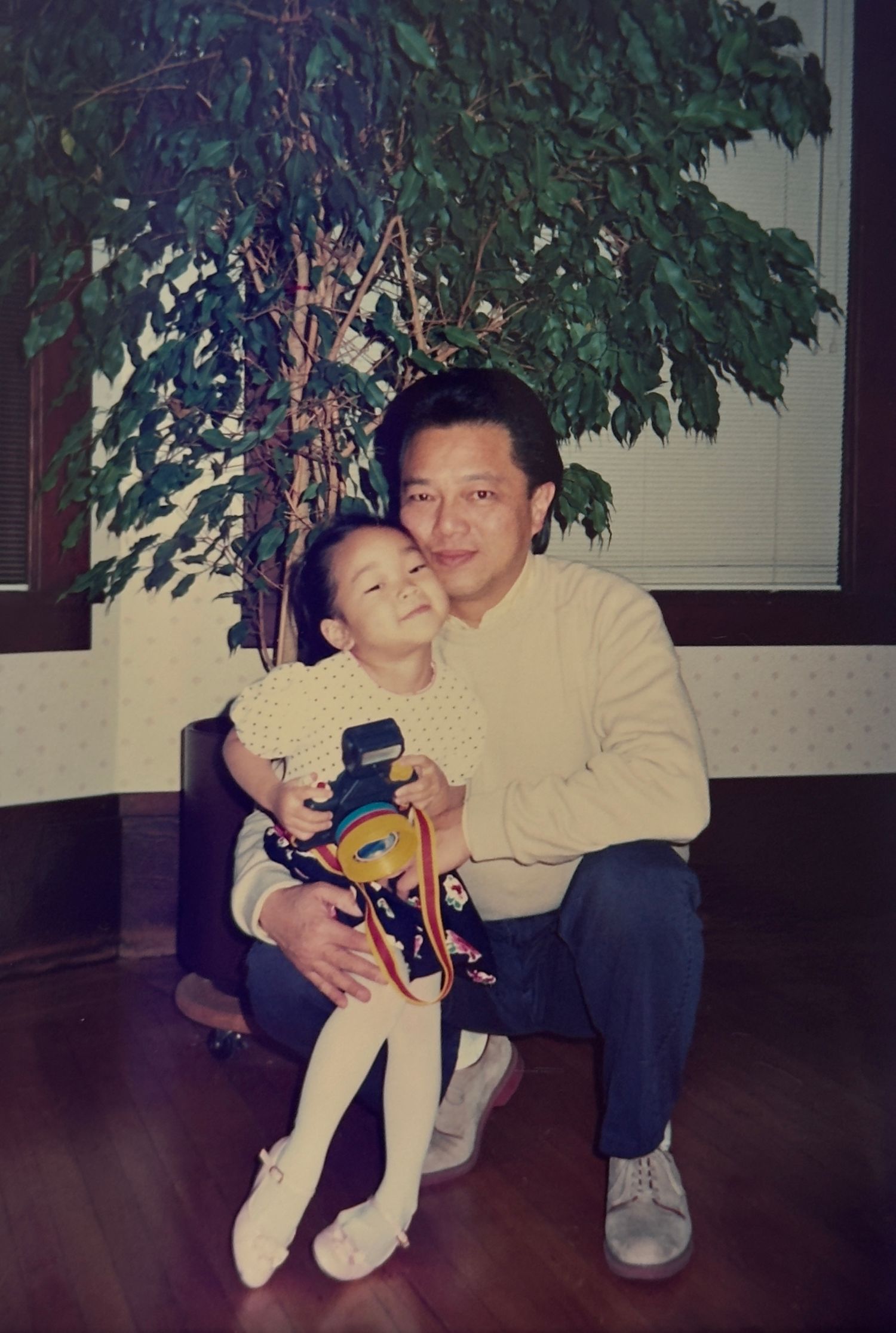 A vintage photo showing two people sitting together indoors next to a potted plant in the 1990s.